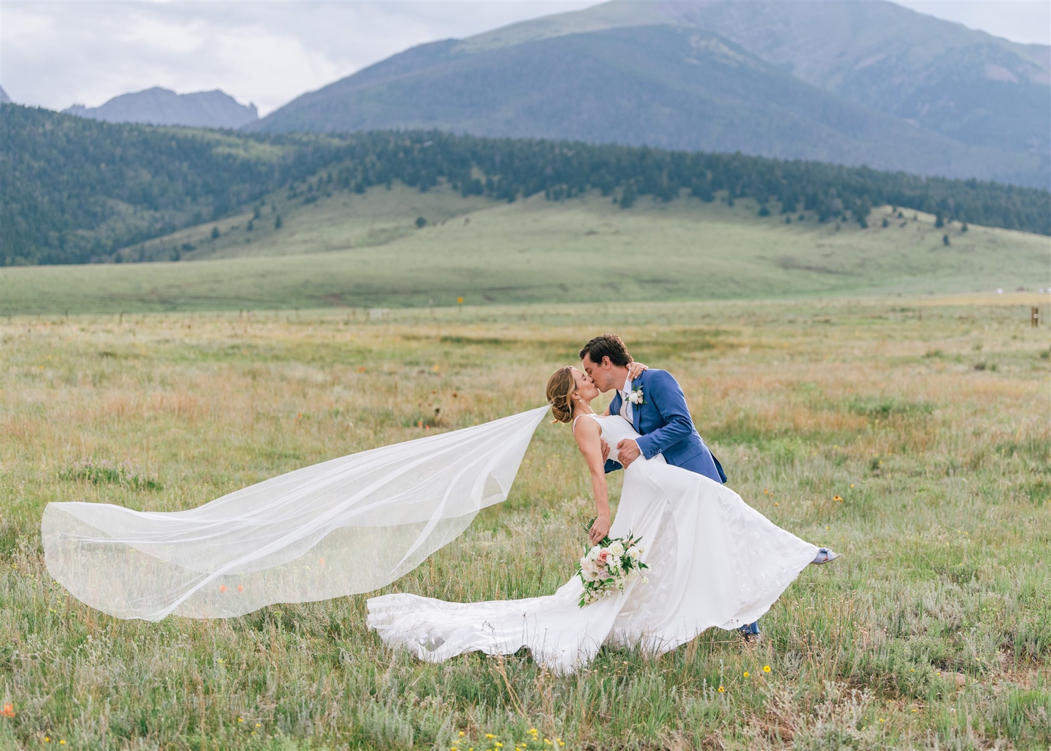 Groom kissing bride with veil flowing in wind for Colorado destination wedding