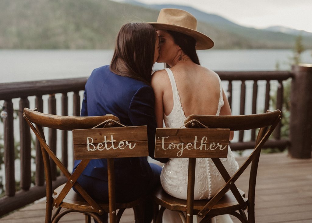 Partners sitting on chairs and kissing with signs that say better together | McArthur Weddings and Events