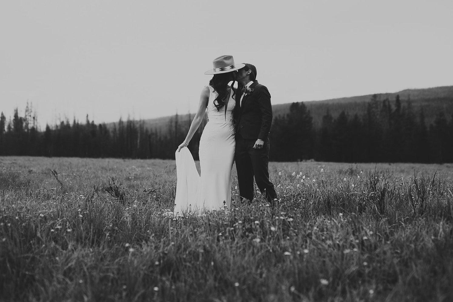 Partners standing in field and kissing at Colorado Airbnb wedding | McArthur Weddings and Events