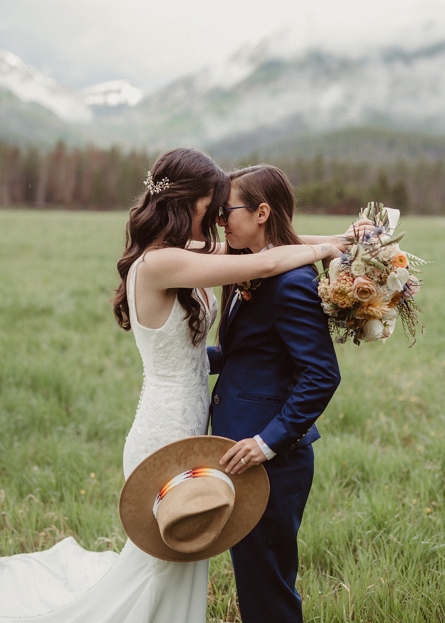 Partner holding bouquet while other partner holds hat as they look at each other | McArthur Weddings and Events
