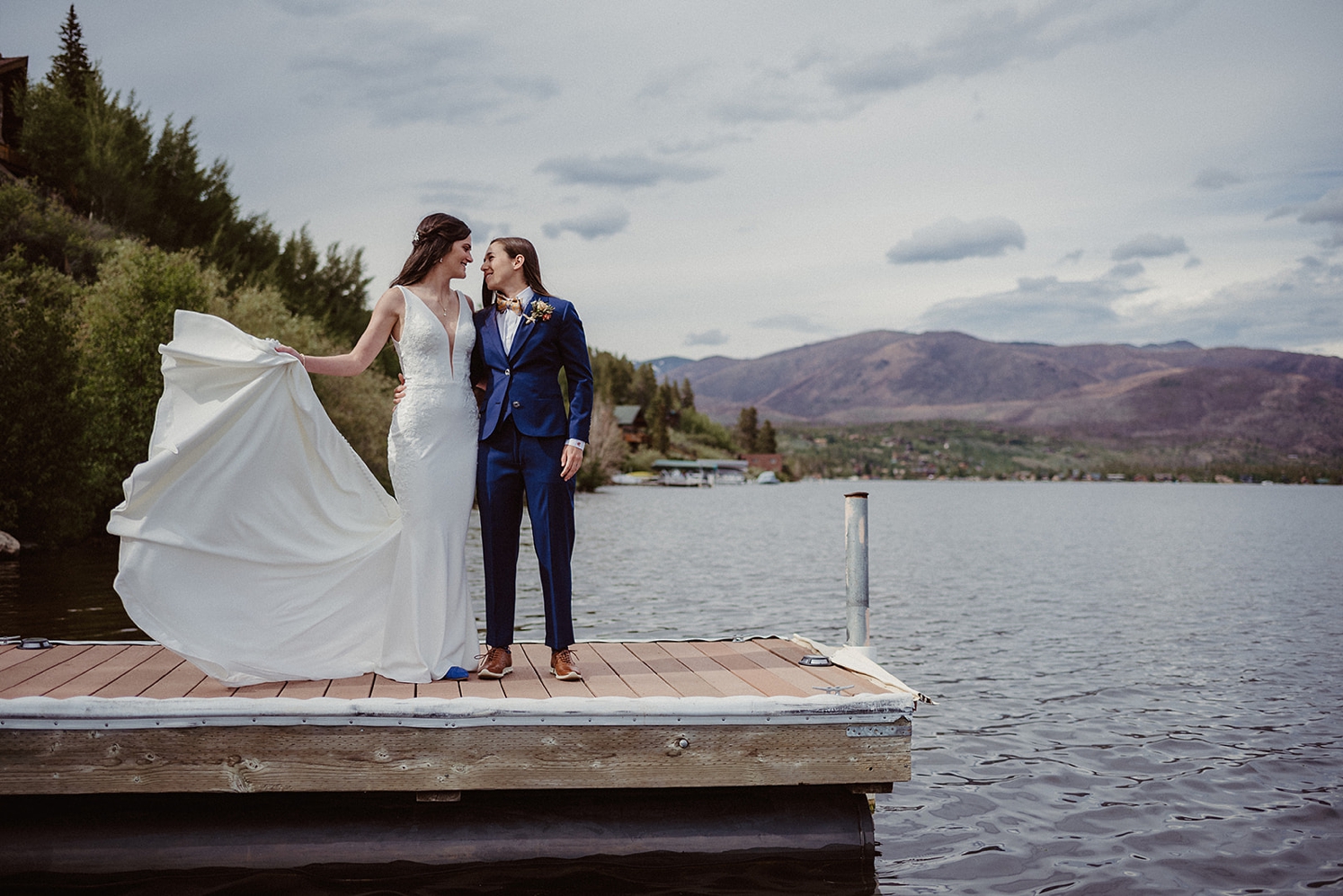 Couple standing on dock with wedding dress train floating in the wind | McArthur Weddings and Events