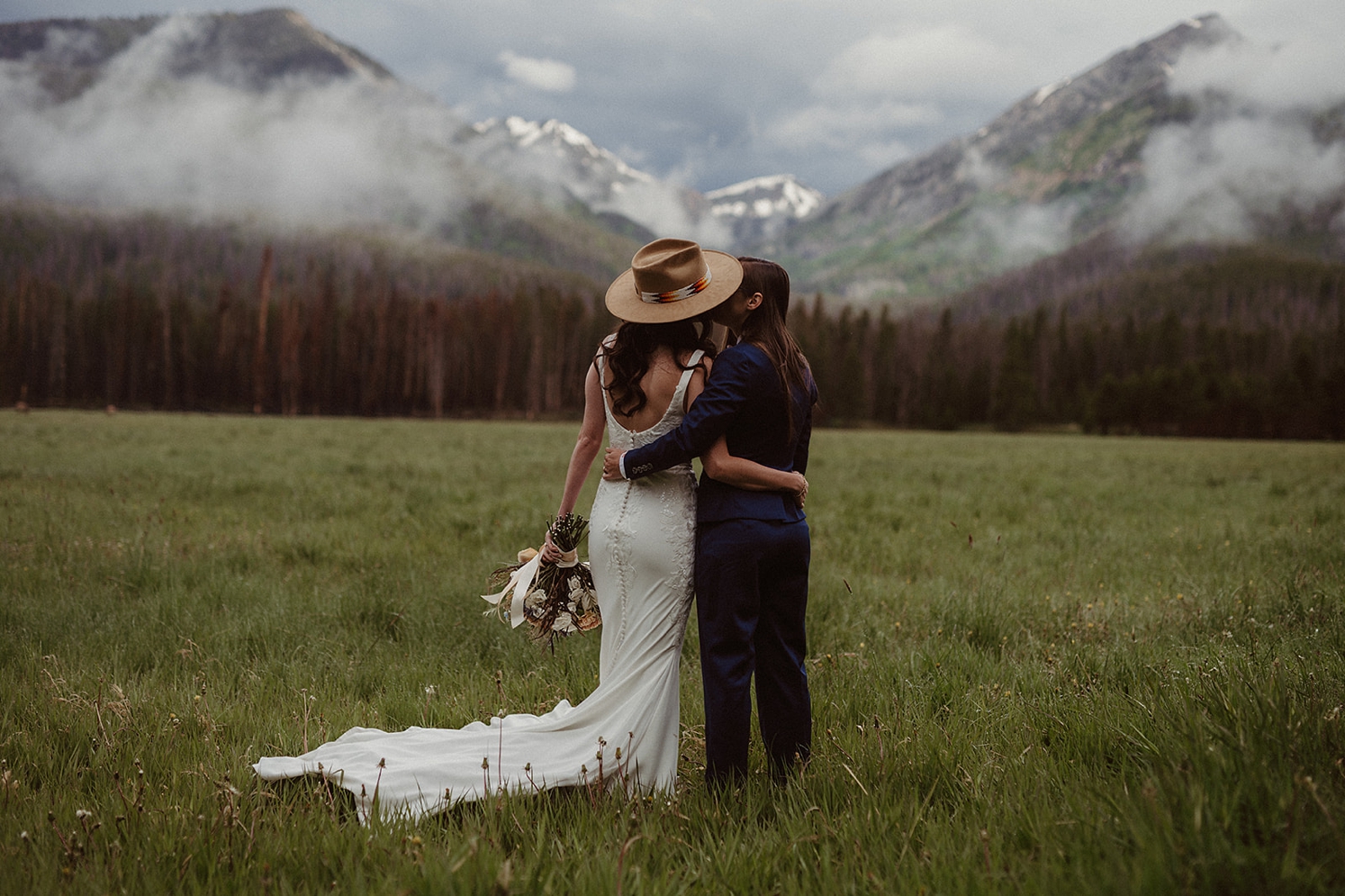 Partners kissing in field in front of mountains at Colorado Airbnb wedding | McArthur Weddings and Events