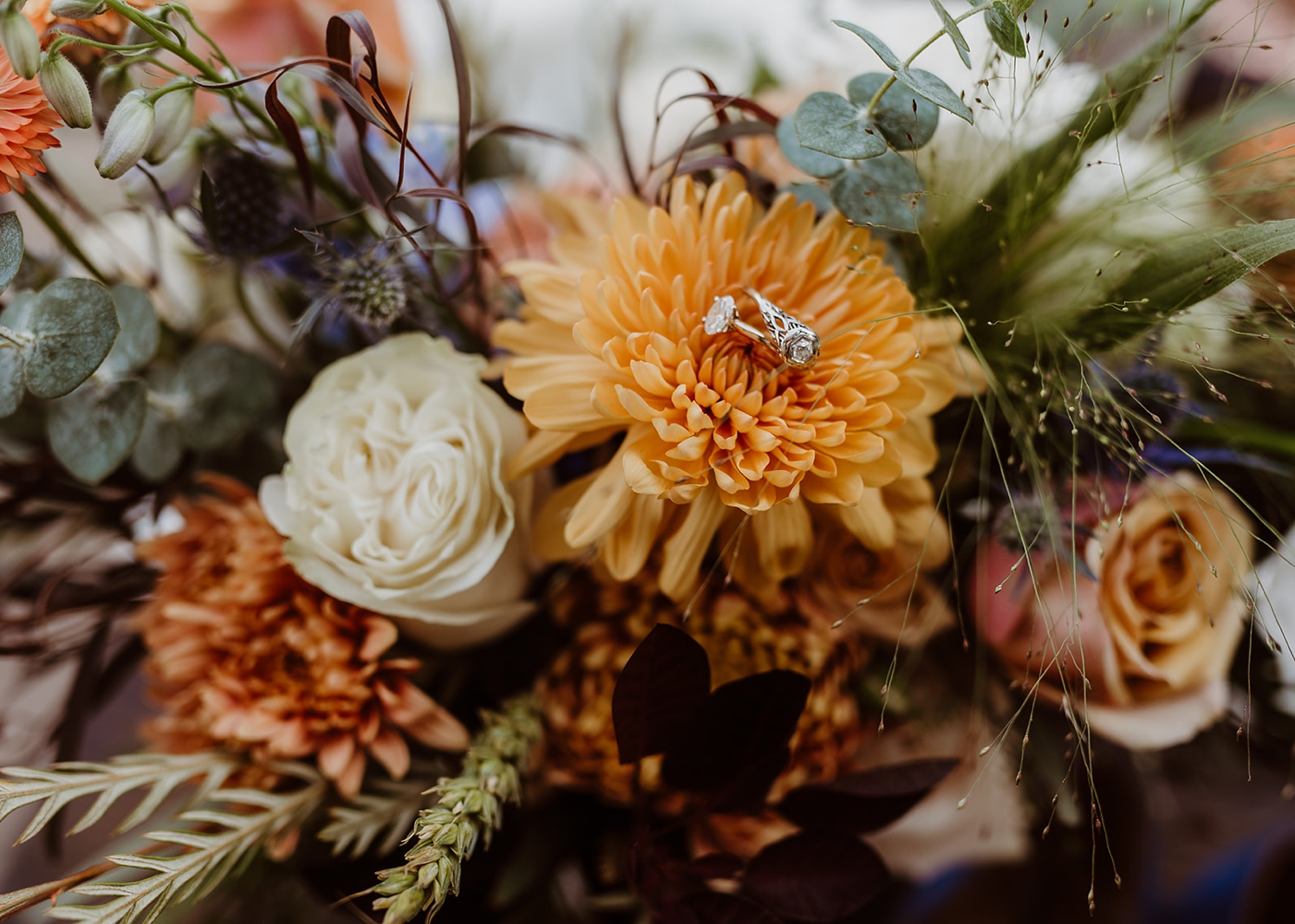 Wedding rings nestled in wedding bouquet on top of orange flower | McArthur Weddings and Events