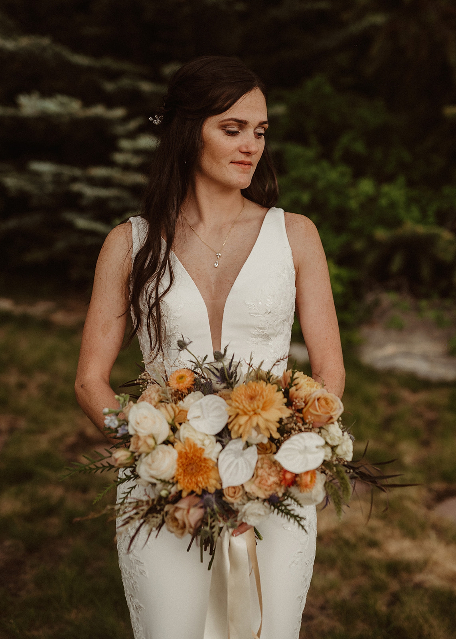 Partner holding bouquet filled with orange and white flowers looking down | McArthur Weddings and Events