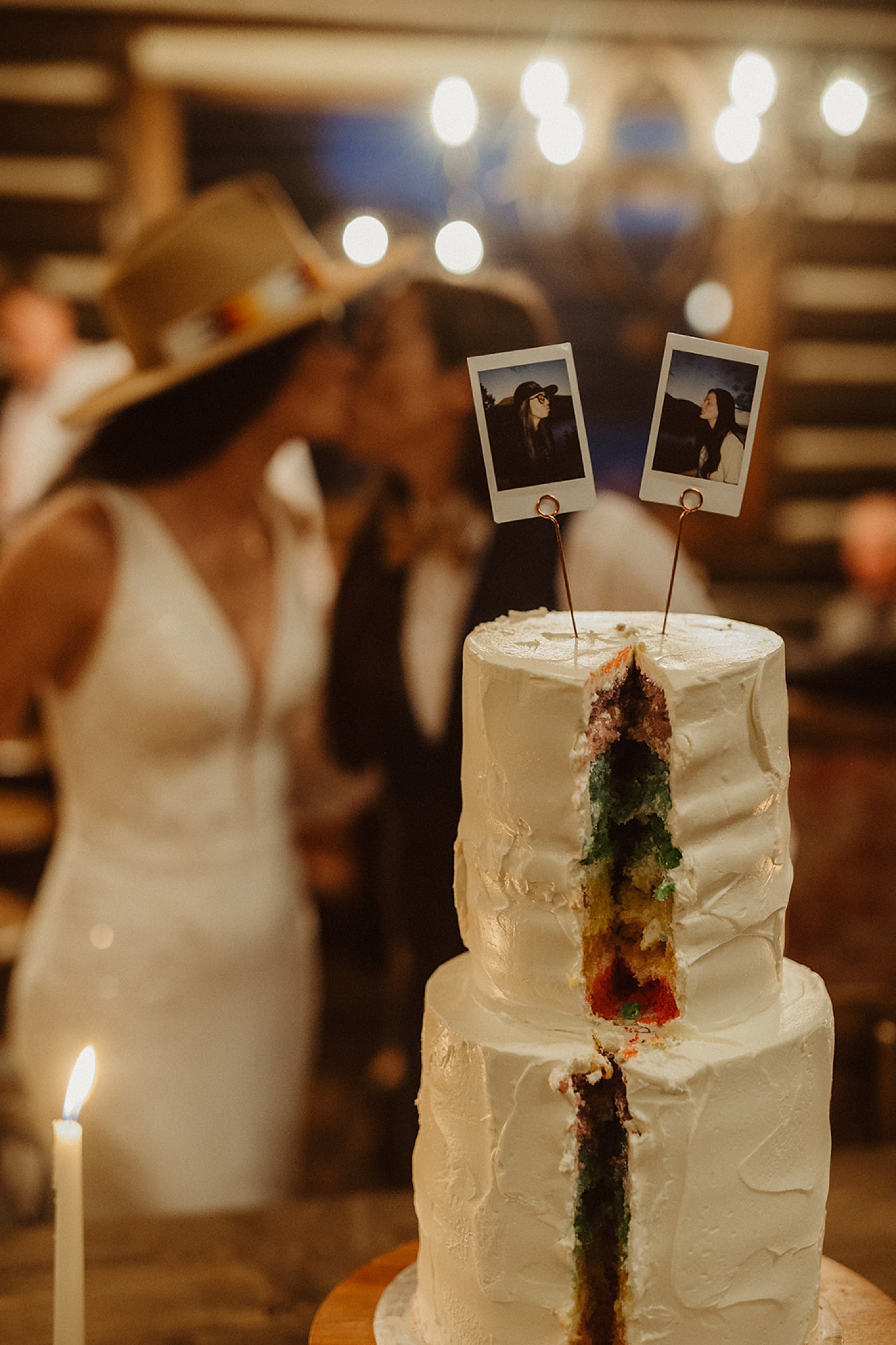 Rainbow wedding cake with partners kissing in the background at Colorado Airbnb wedding | McArthur Weddings and Events