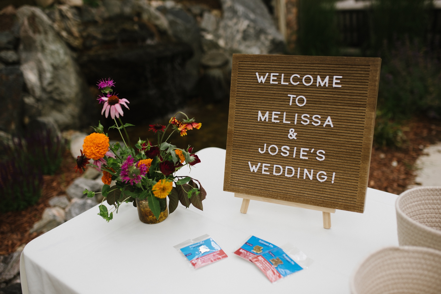 Welcome table with bright flower and pronoun pins at LGBTQ wedding | McArthur Weddings and Events