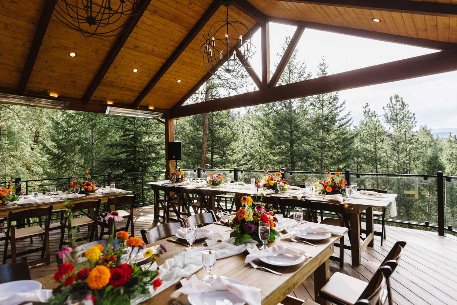 Bright, colorful floral arrangements set up on tables on outdoor deck at wedding reception at Juniper Mountain House | McArthur Weddings and Events