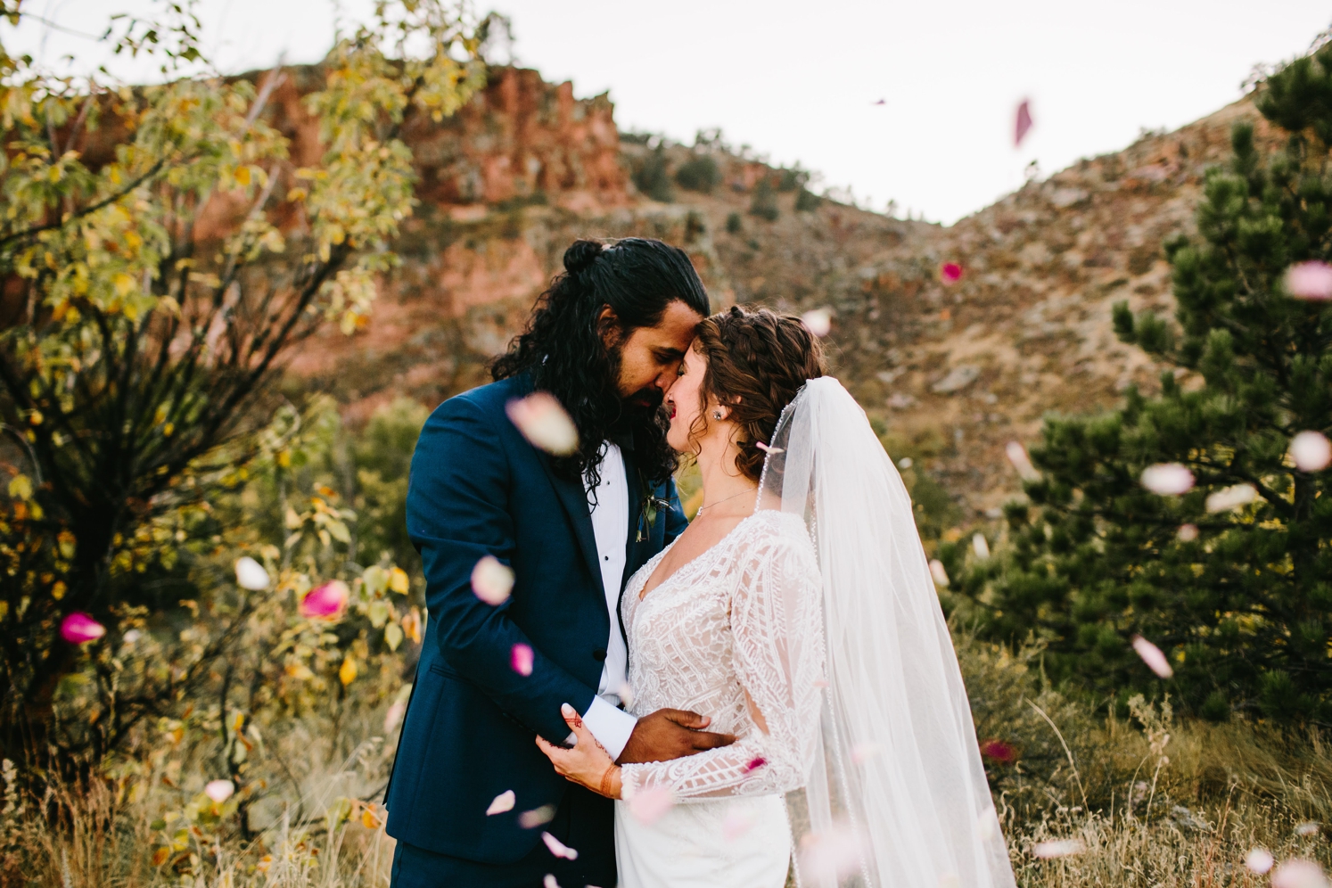 Couple kissing after wedding in Colorado with rose petals being thrown in the air | McArthur Weddings and Events