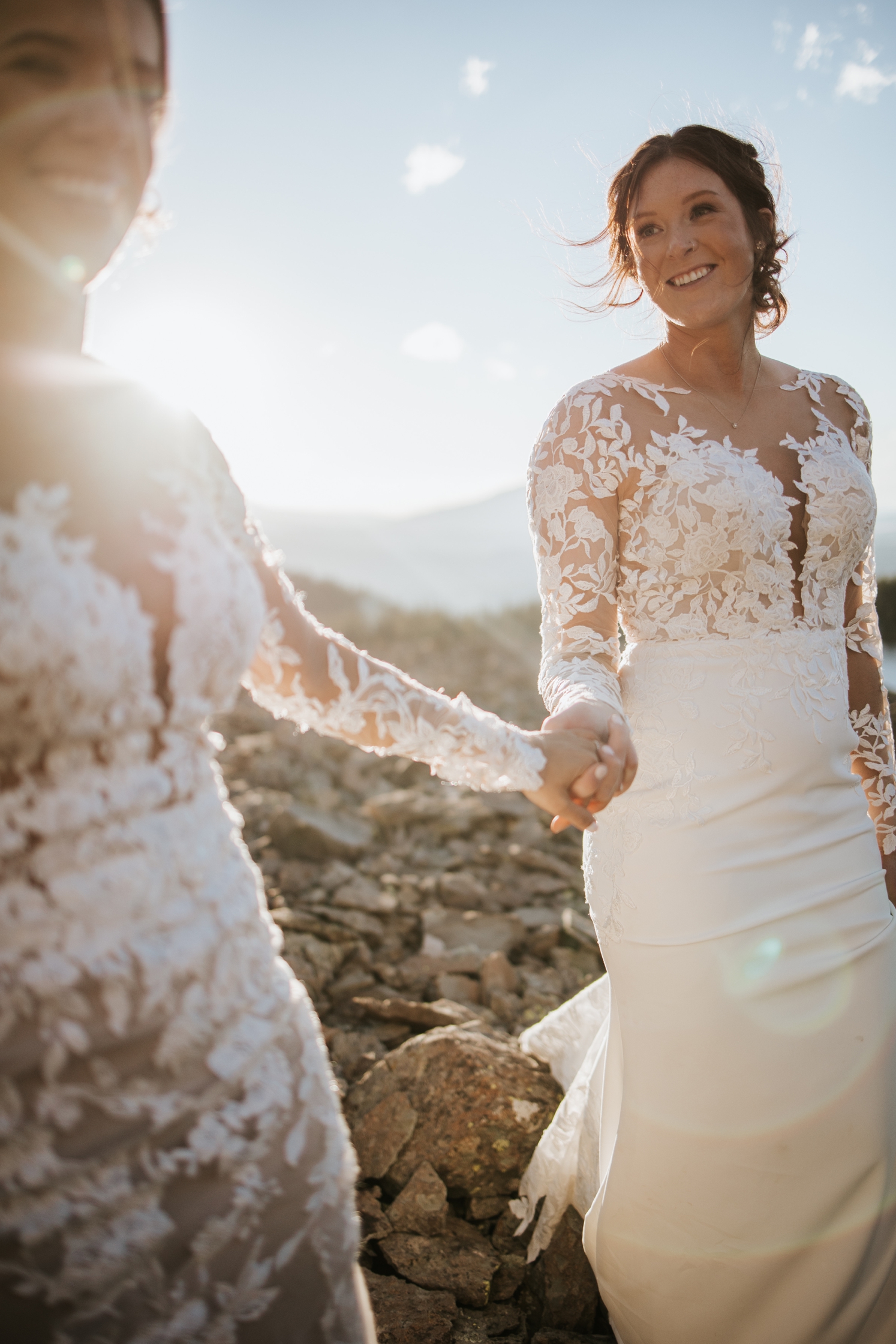 Brides walking on mountain and holding hands during golden hour | McArthur Weddings and Events