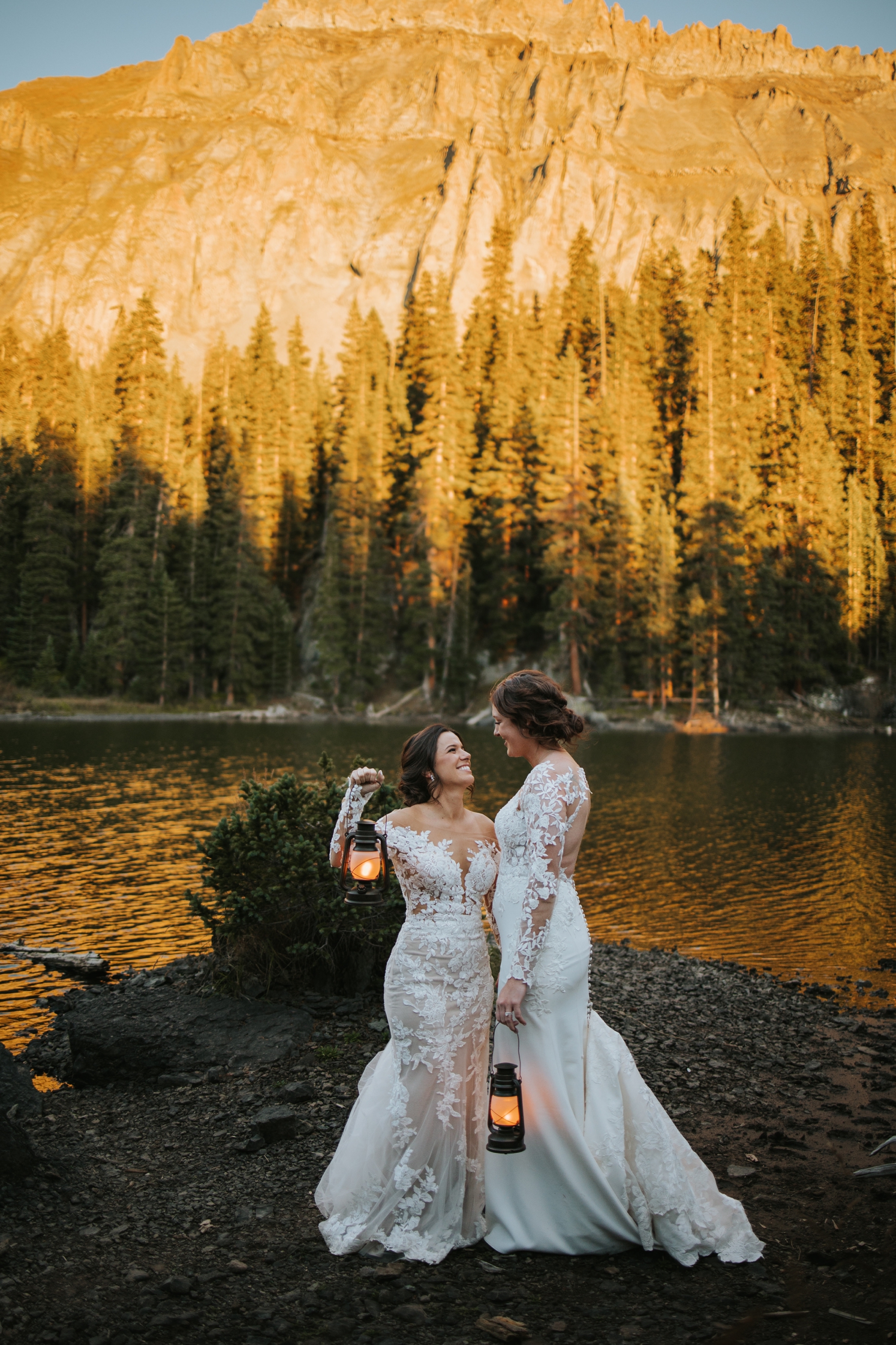 Partners holding lanterns and standing lakeside at Telluride wedding | McArthur Weddings and Events