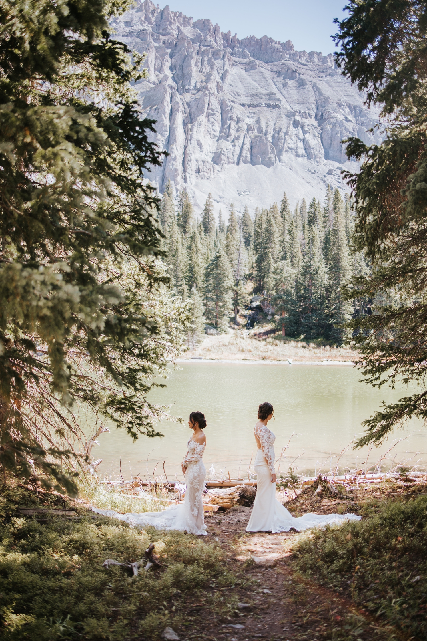 Two brides standing in front of lake facing away from each other before first look at Telluride wedding | McArthur Weddings and Events