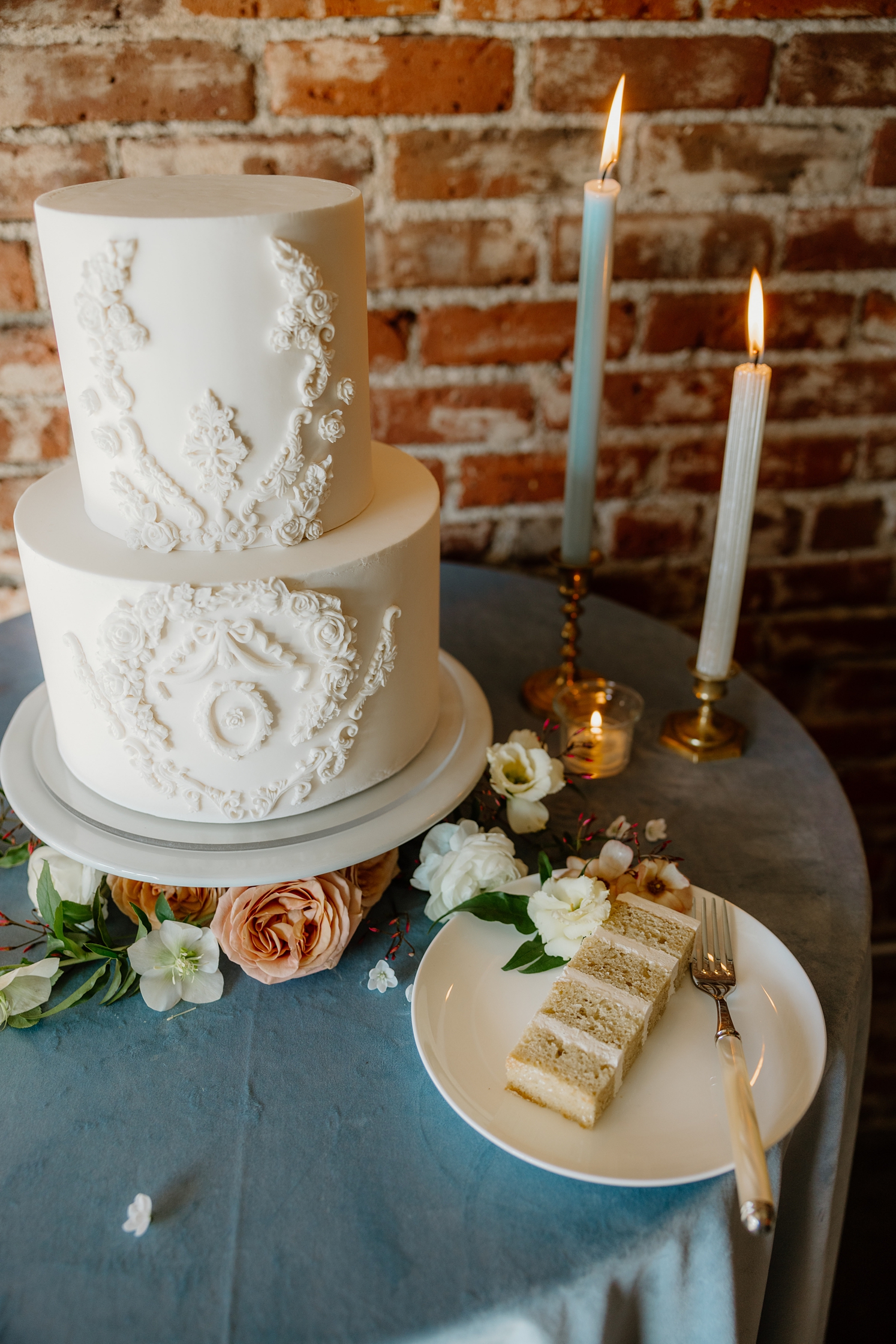 Two tier white wedding cake with ornate details next to candles | McArthur Weddings and Events