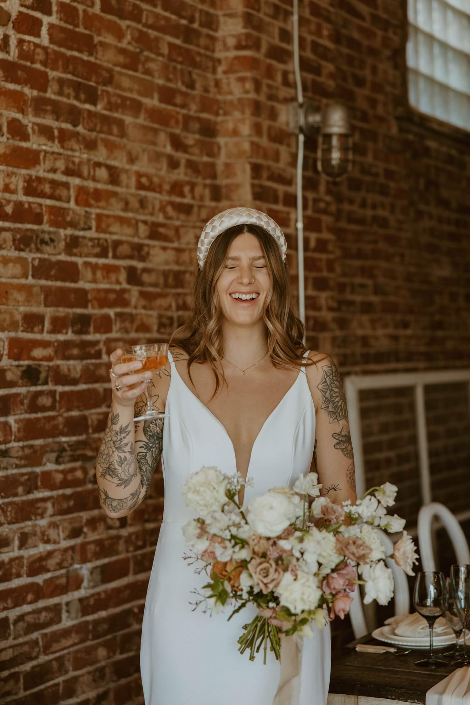 Bride wearing statement headband laughing and holding champagne | McArthur Weddings and Events