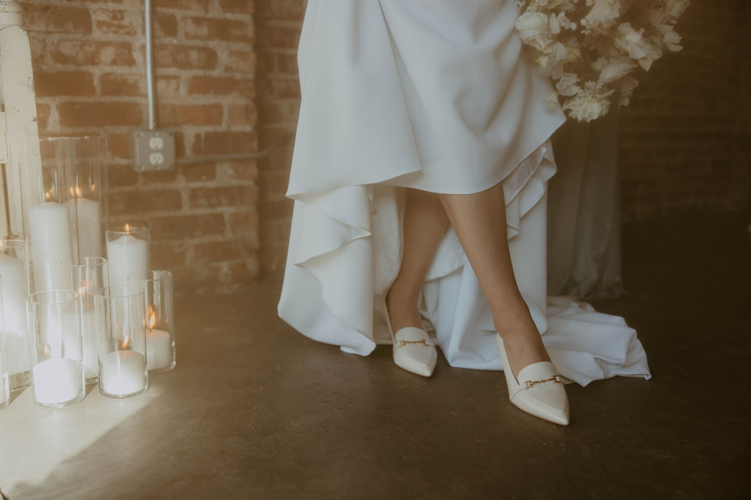 Bride lifting up dress to show off white shoes next to white candles | McArthur Weddings and Events