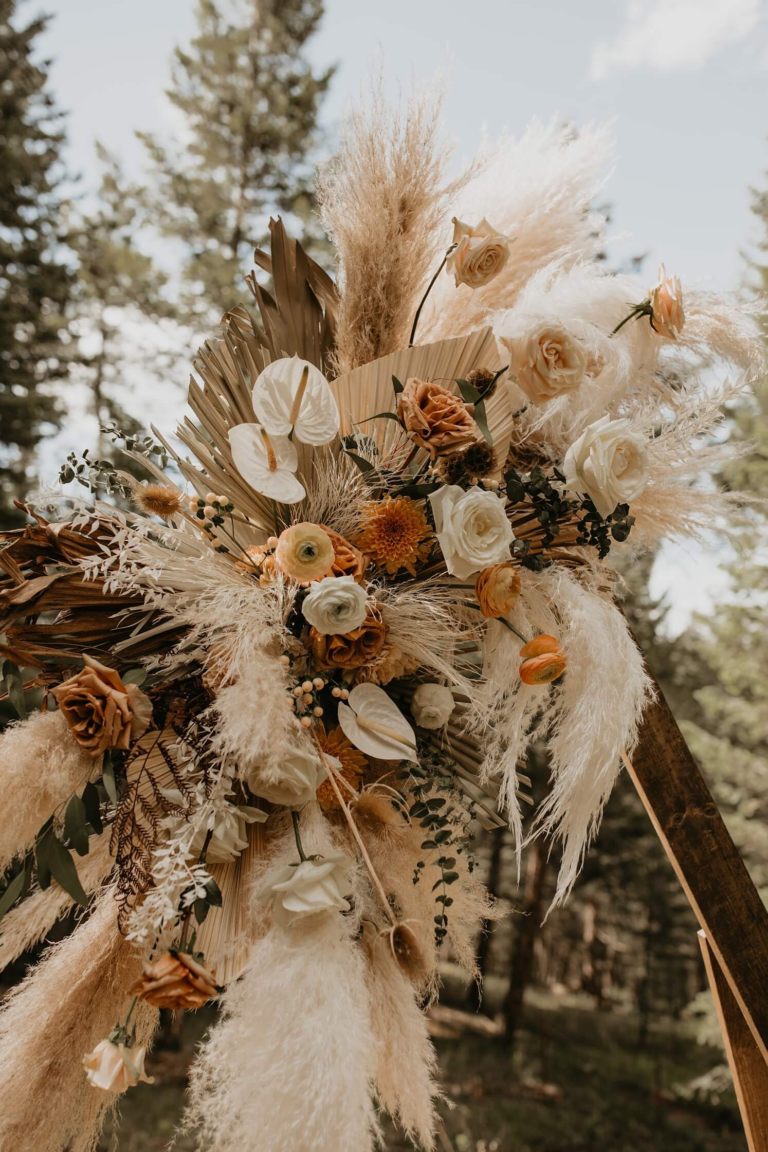 Wedding floral design: boho ceremony florals hanging on arch with pampas grass, fan leaves, and white and burnt orange flowers | McArthur Weddings and Events