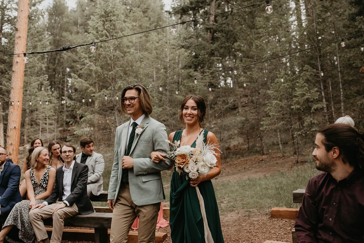 Wedding floral design: groomsman and bridesmaid carrying boho bouquet walking down the aisle | McArthur Weddings and Events