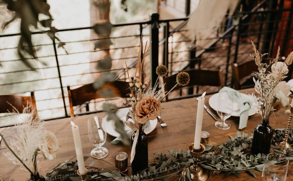 Wedding floral design: Boho flowers in small brown vases with white candles and greenery on reception table | McArthur Weddings and Events