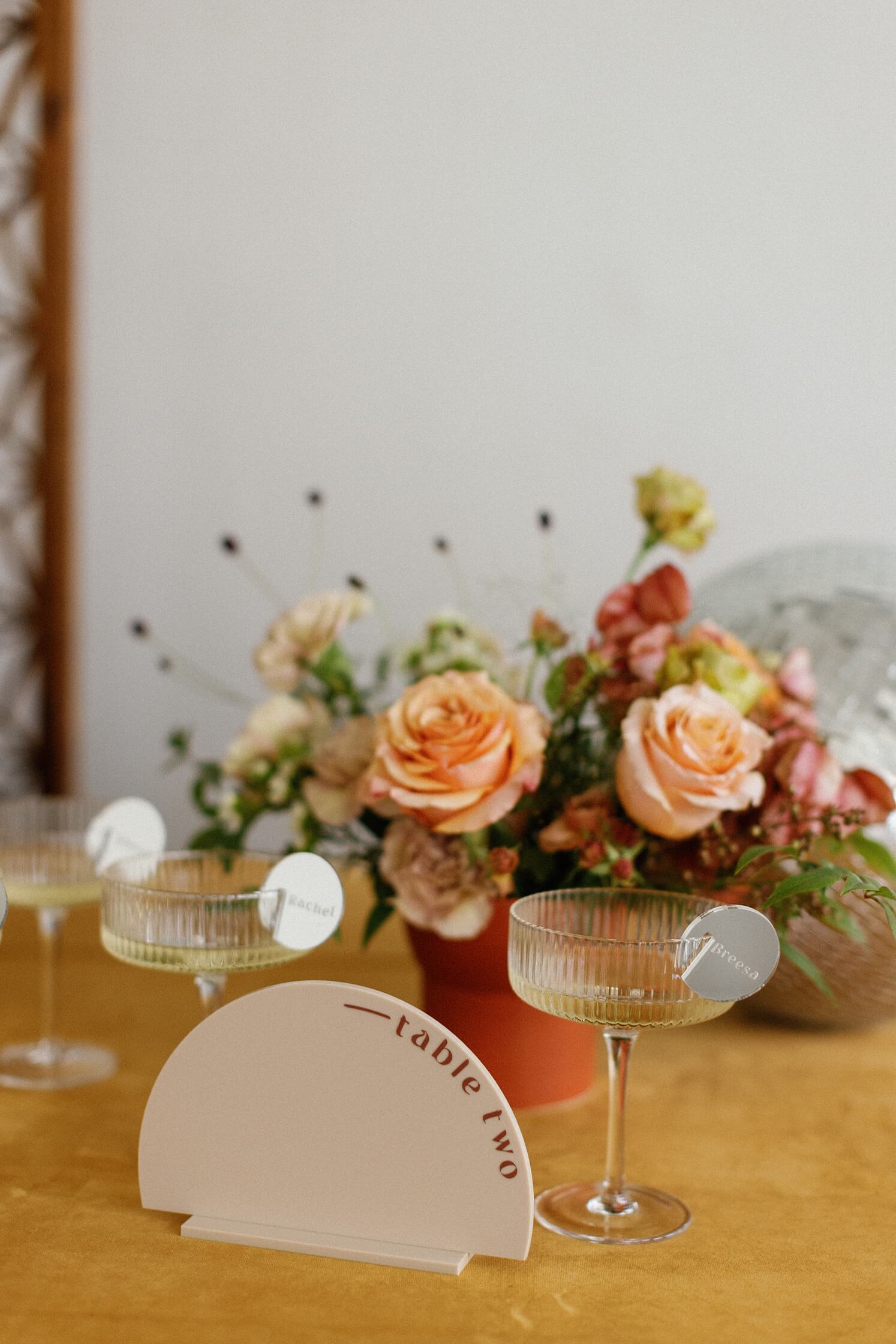 Wooden half circle table numbers with champagne glasses in front of coral flowers | McArthur Weddings and Events