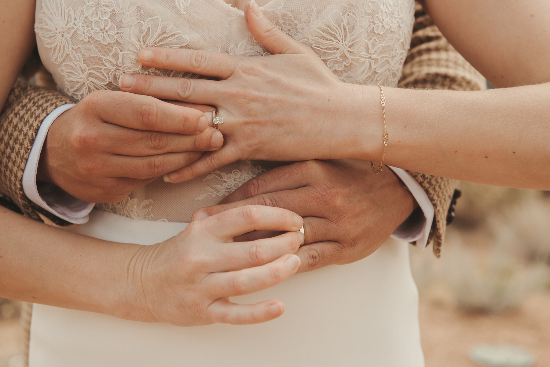 Groom standing behind bride with arms around her while they hold each other's rings