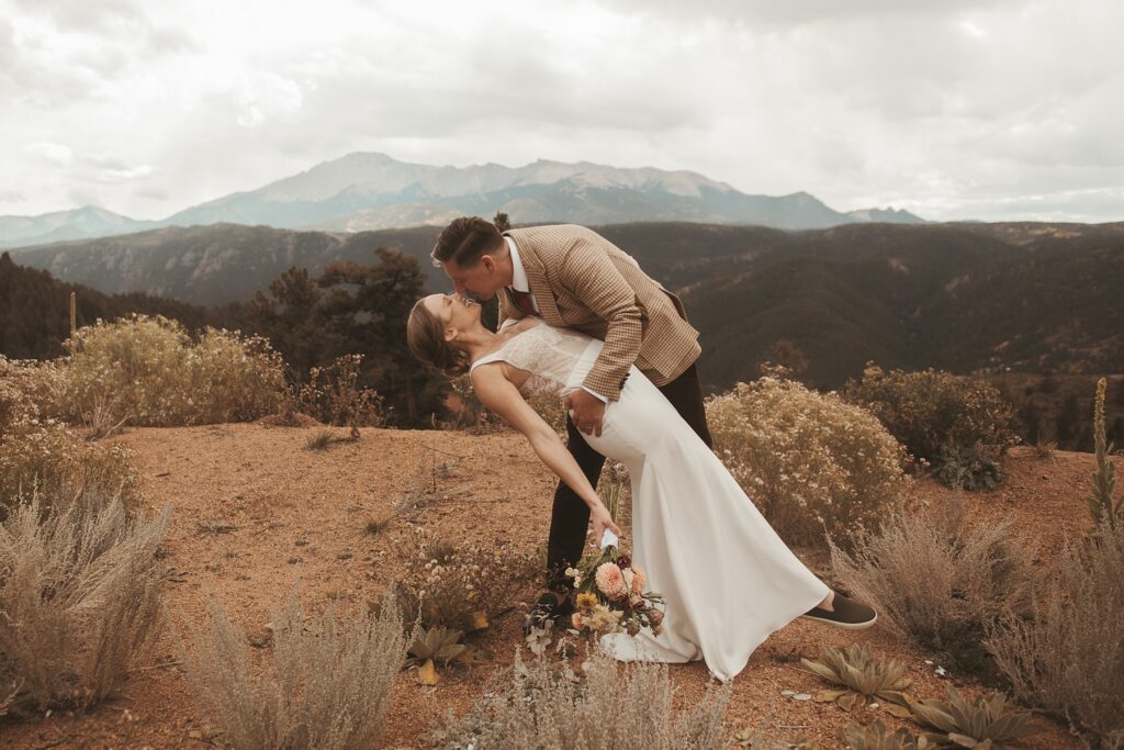 Groom dipping bride for a kiss in front of Colorado mountains