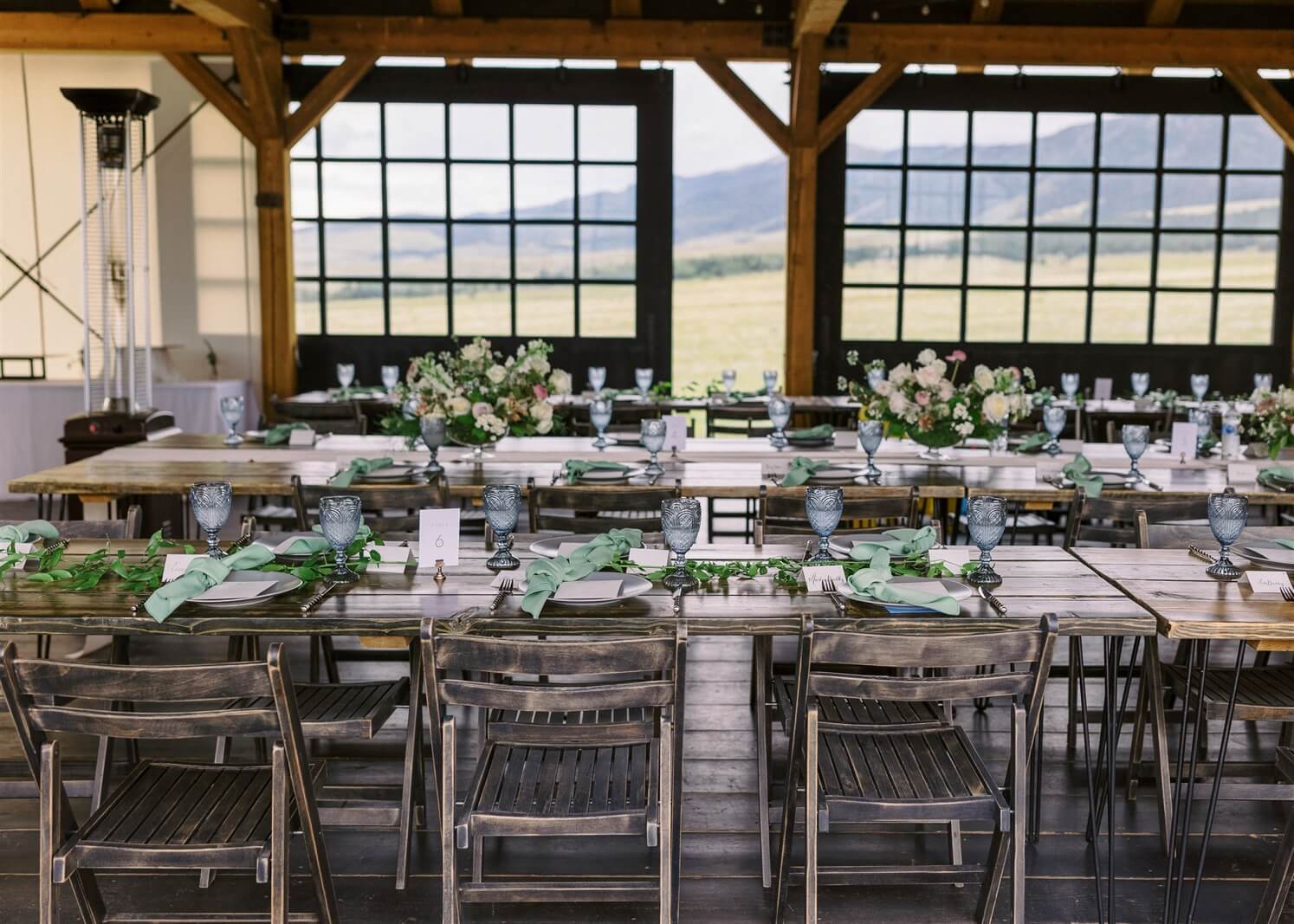 Vintage blue crystal glasses with light green napkins on rustic wood tables at Three Peaks Ranch in post about true cost of a wedding venue