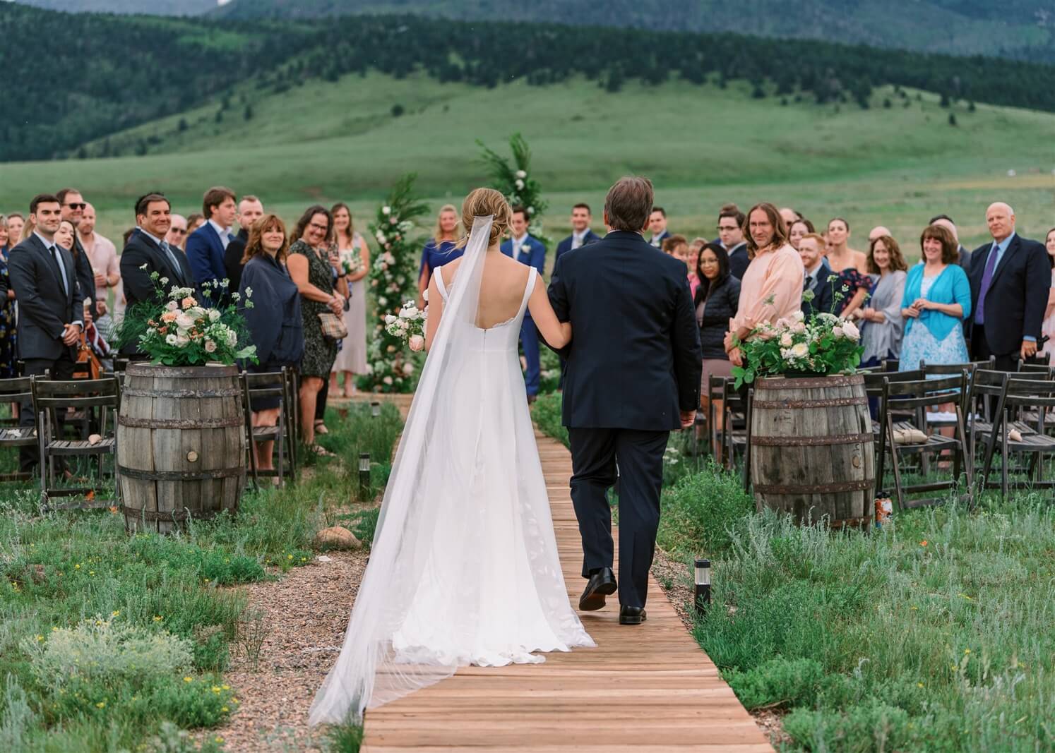 Bride walking down the aisle with her father at Three Peaks Ranch in post about true cost of a wedding venue