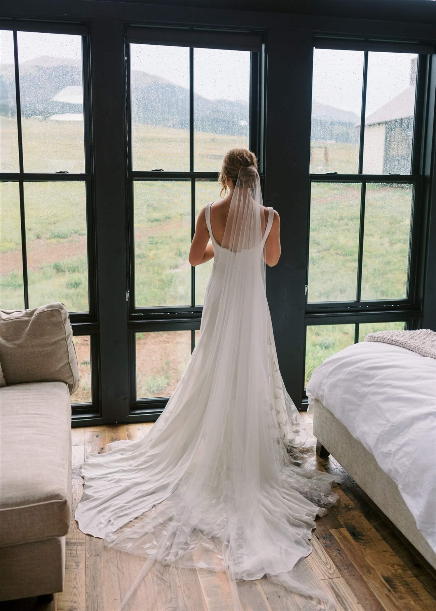 Bride looking out the window in her dress at Three Peaks Ranch in post about true cost of a wedding venue