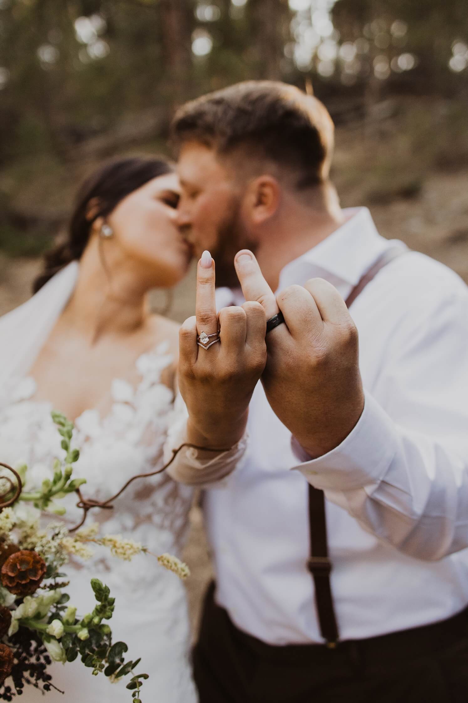 Bride and groom sticking up ring fingers and kissing at Evergreen wedding venue | McArthur Weddings and Events