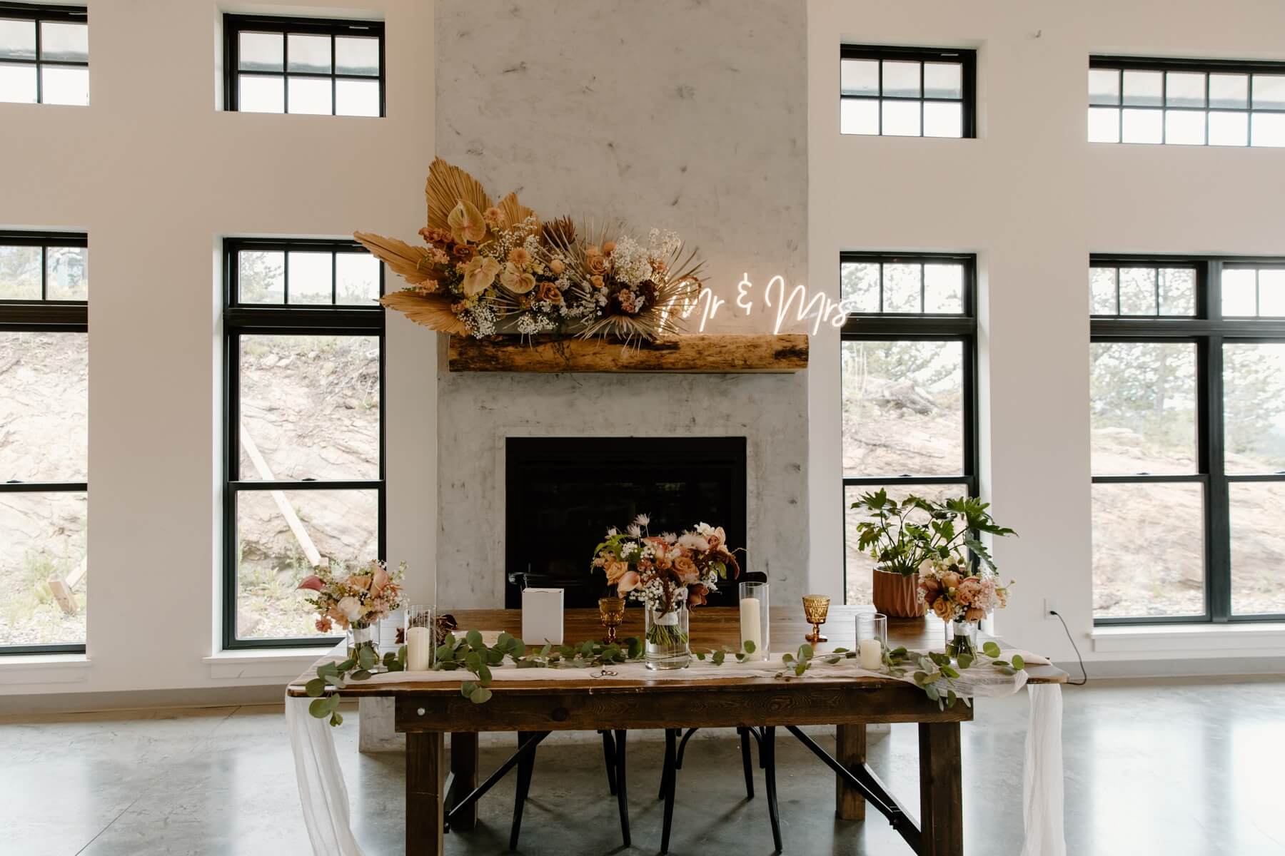 Sweetheart table with boho floral arrangement and neon sign on the mantle behind the table | McArthur Weddings and Events