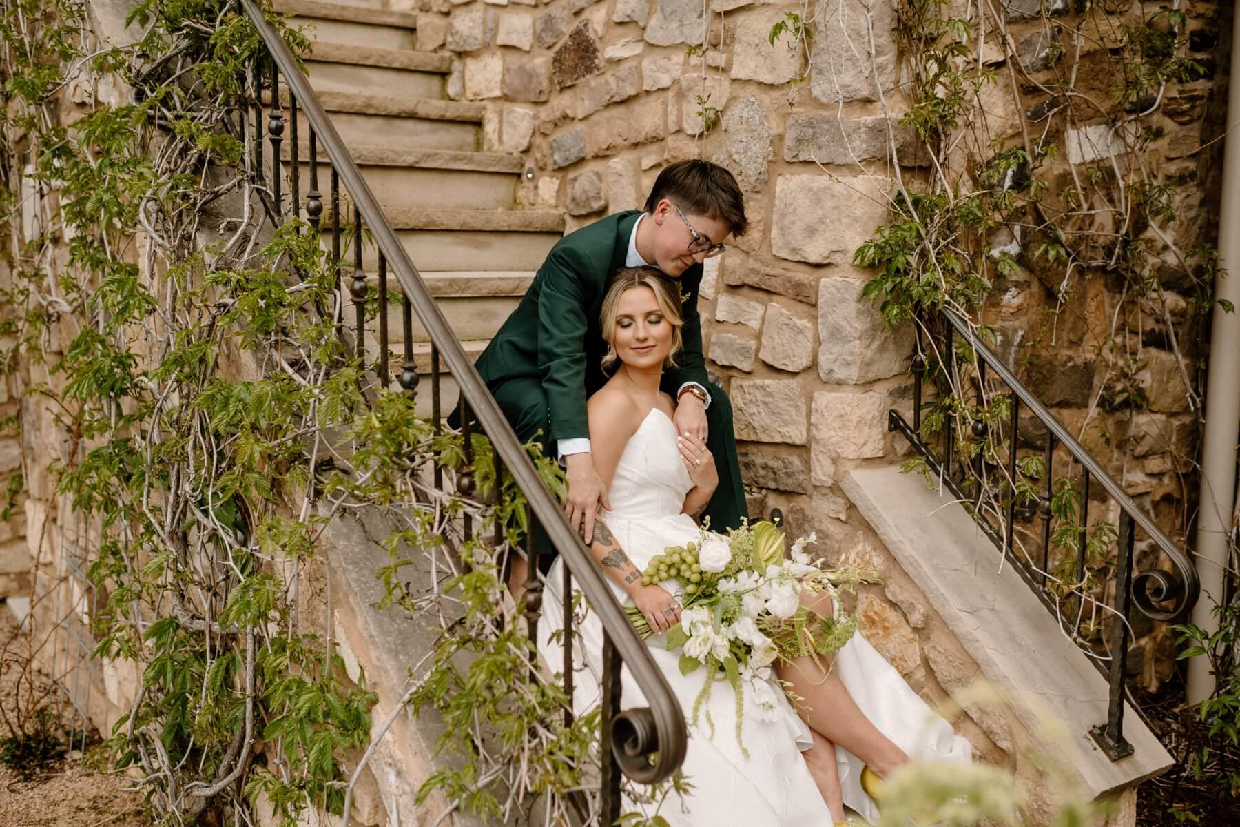 Couple sitting on stone steps in wedding dress and dark green suit