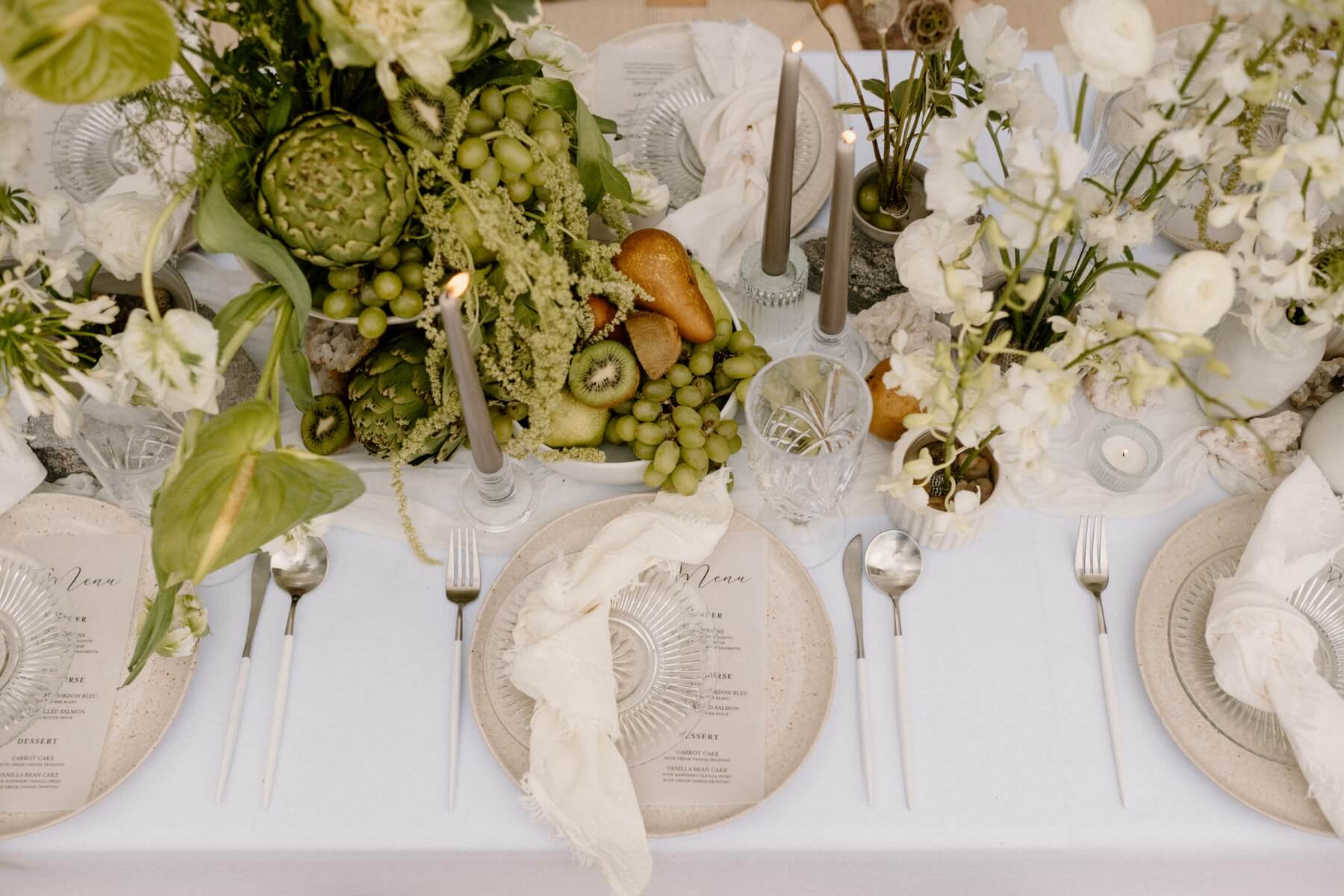 Round stone colored plates with menus, cream napkins, and green and white florals with fruit