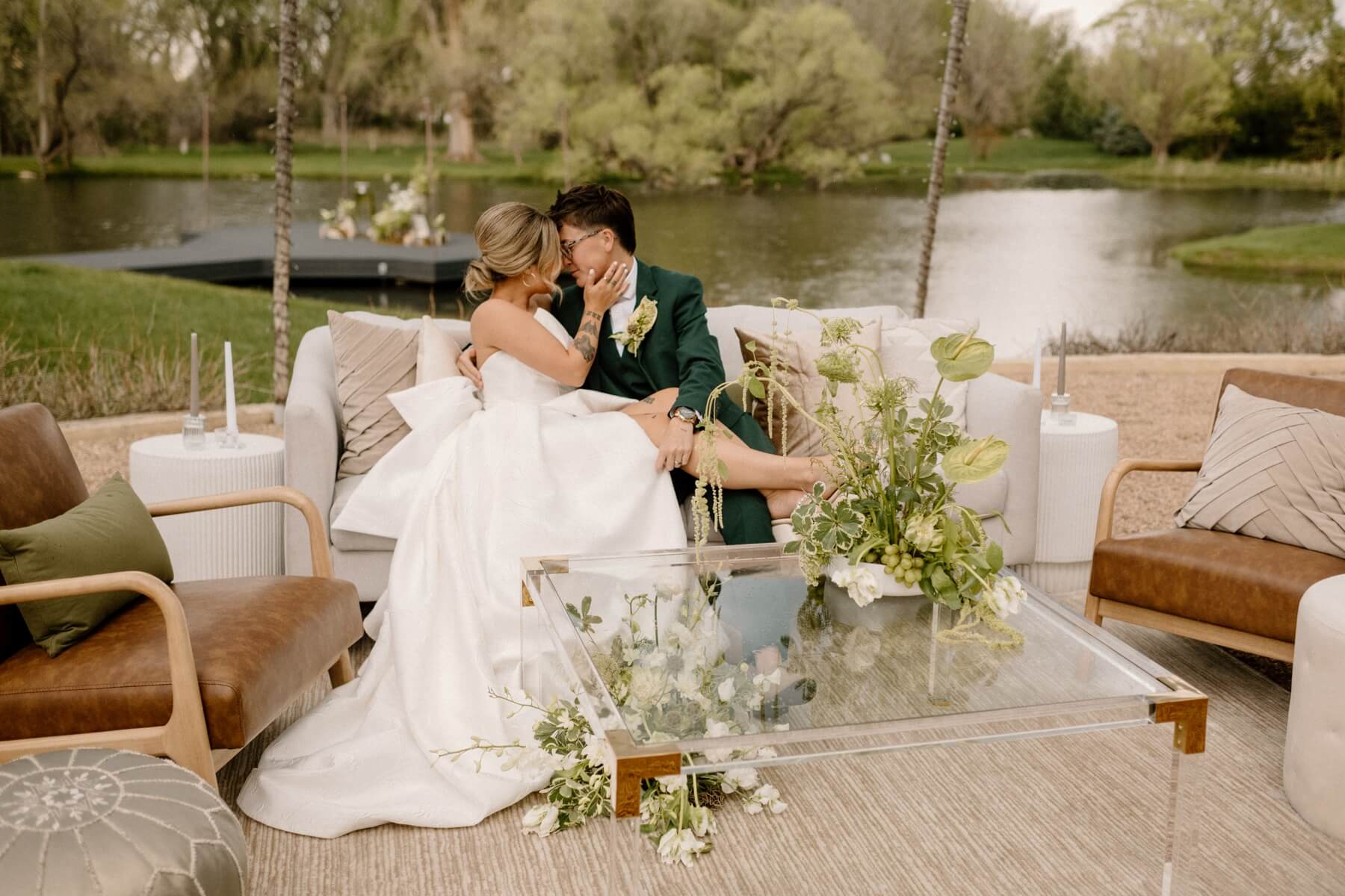 Partners sitting on lounge set with green and white wedding flowers in front of them
