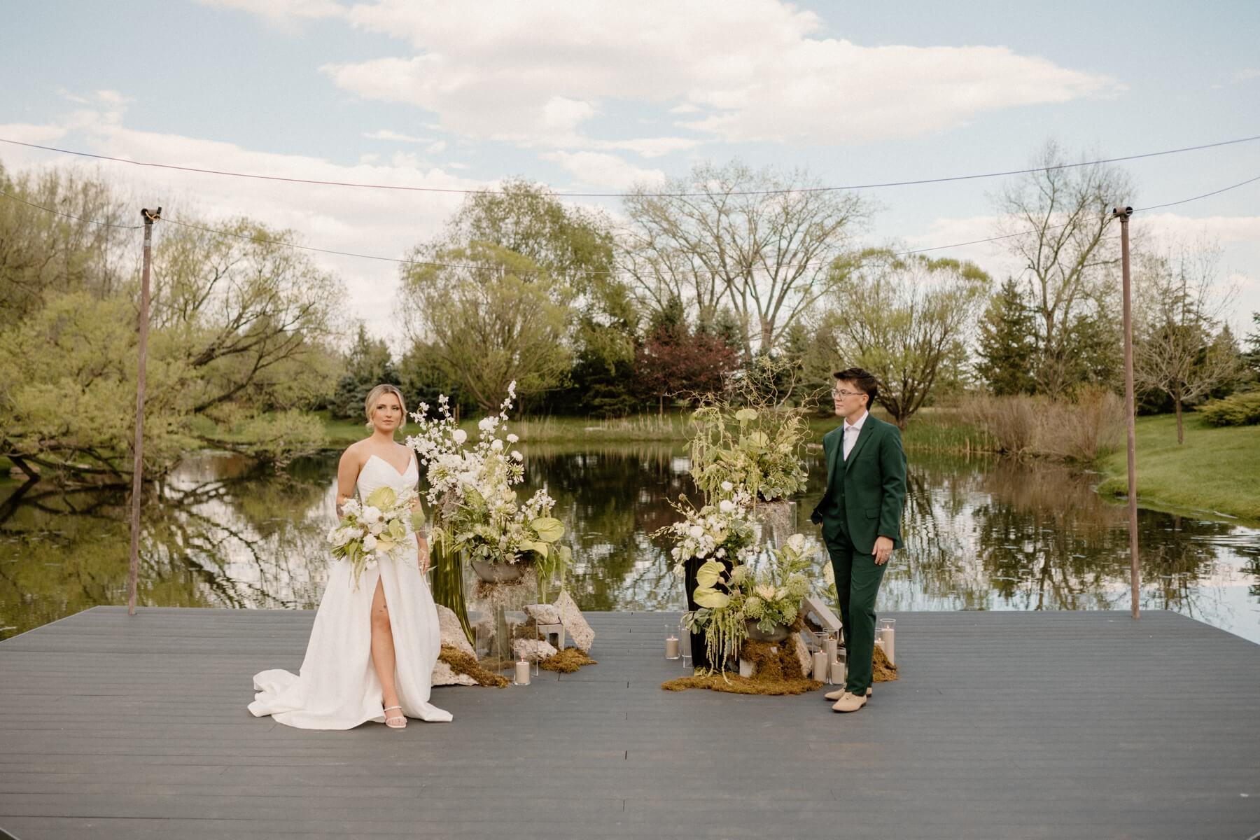 Couple standing on dock in front of green and white wedding flowers with stone and moss elements