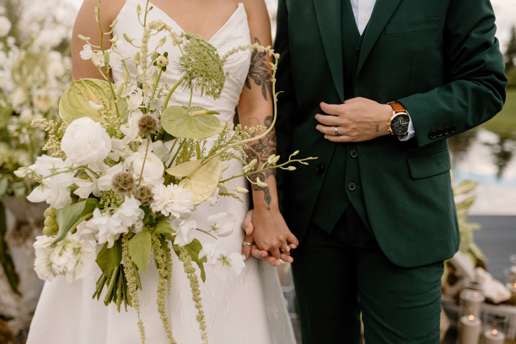 Partner's holding hands with green and white wedding bouquet in front