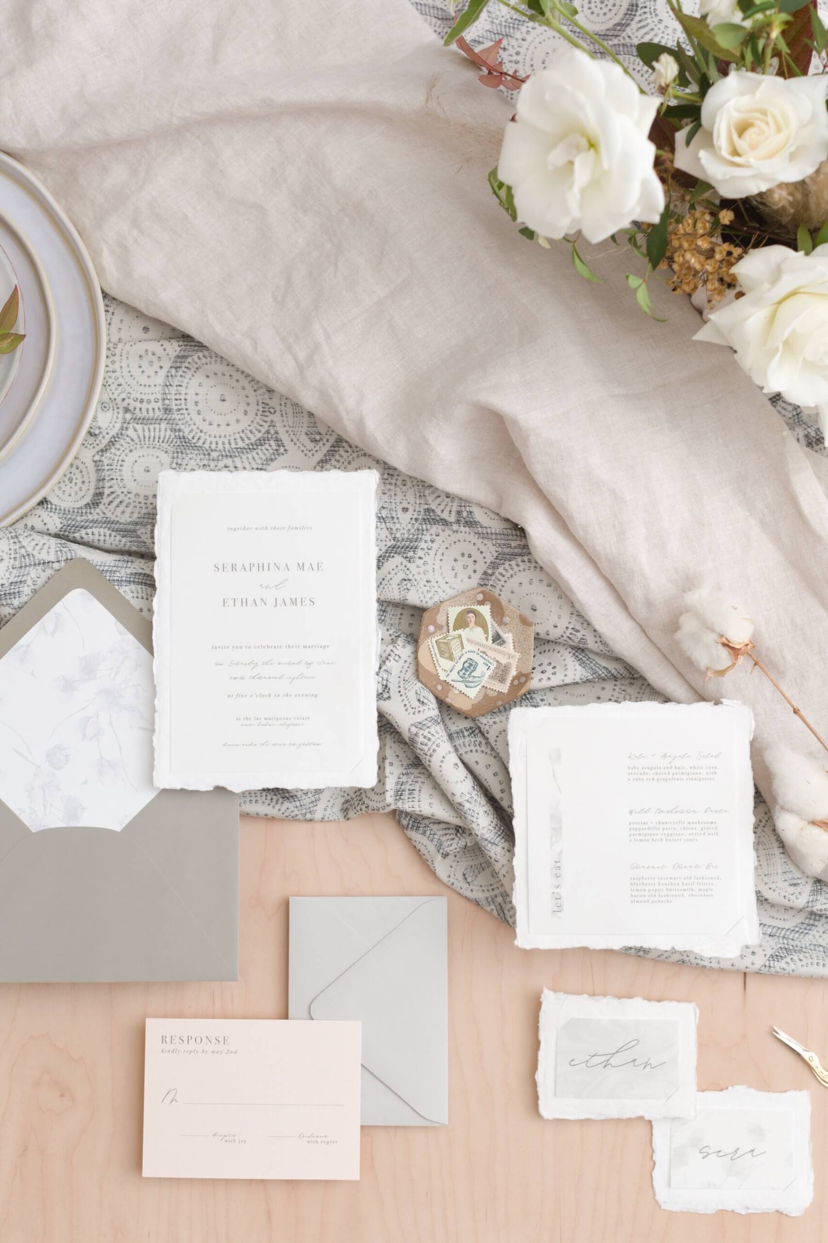 Invitation flat lay with vintage stamps, patterned fabric, and white flowers