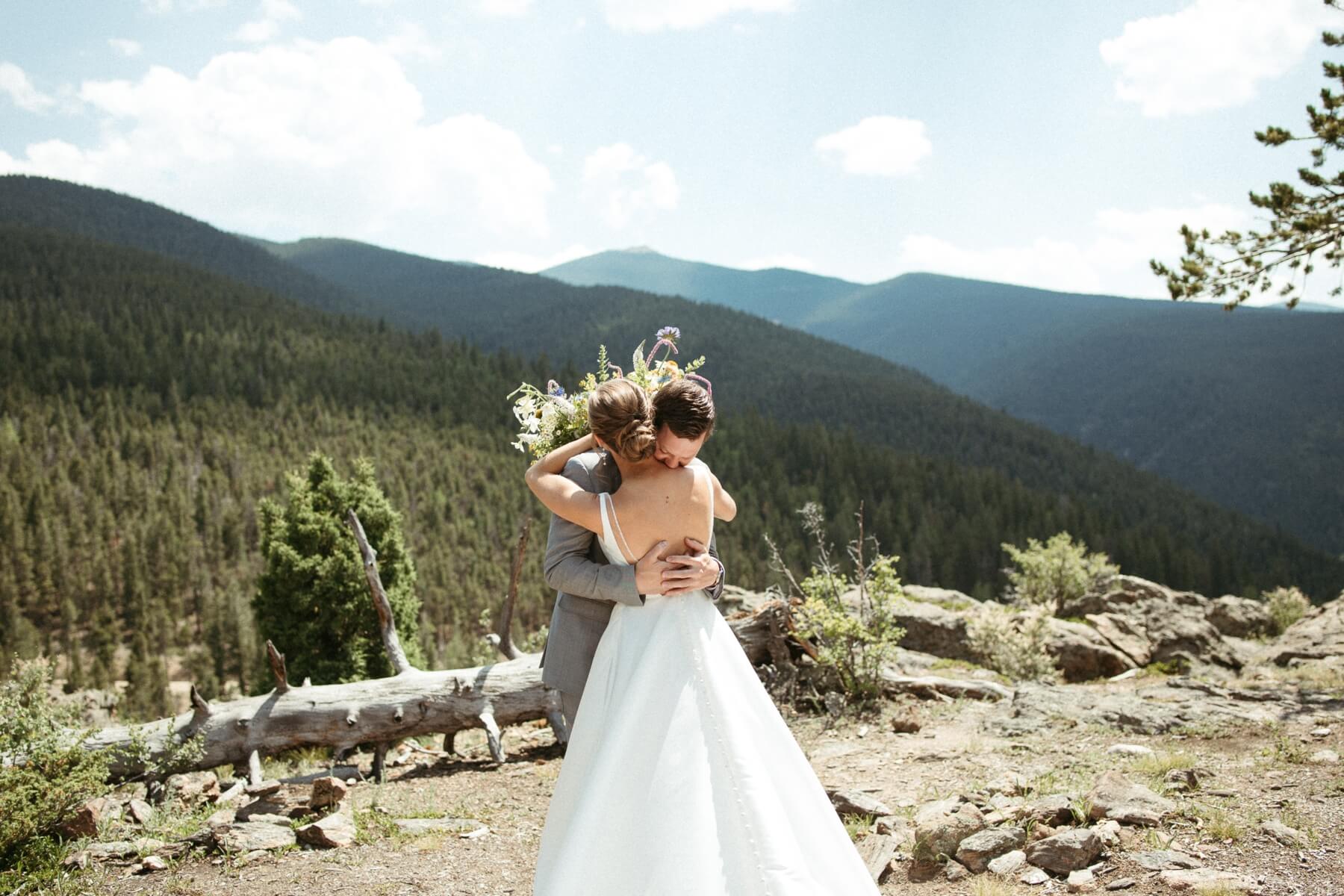 Bride and groom hugging during first look at overlook with mountains behind them