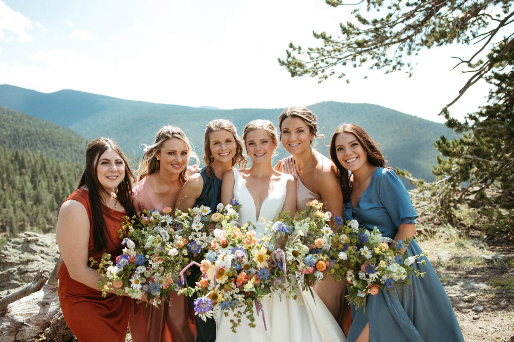 Bride with bridesmaids wearing different colored dresses and holding colorful bouquets at North Star Gatherings, a Colorado mountain wedding venue
