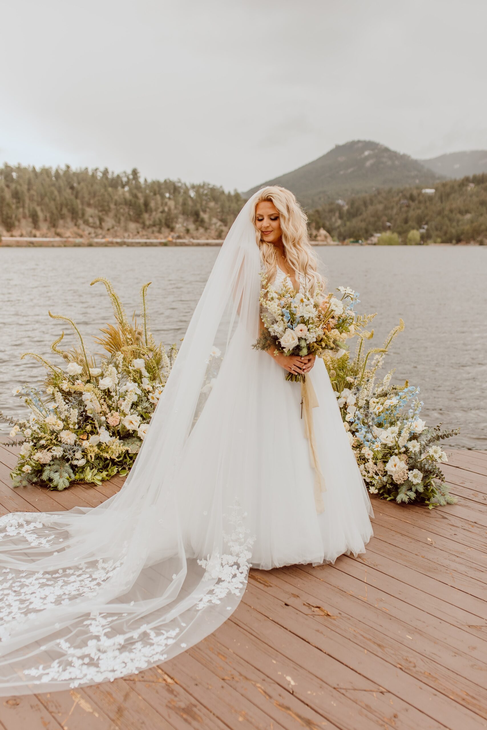 Bride holding wildflower bouquet in front of grounded floral arch and lake