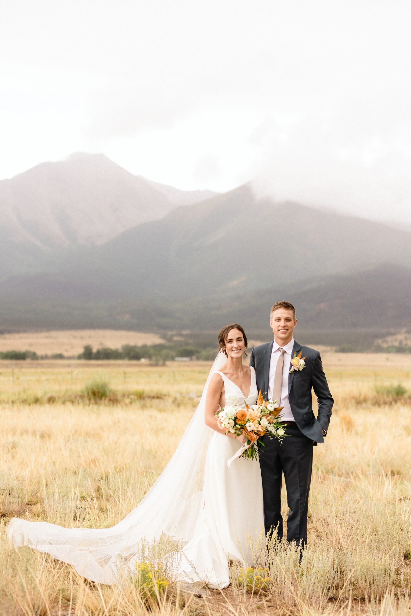 Bride and groom standing in field in front of mountains in Buena Vista, CO