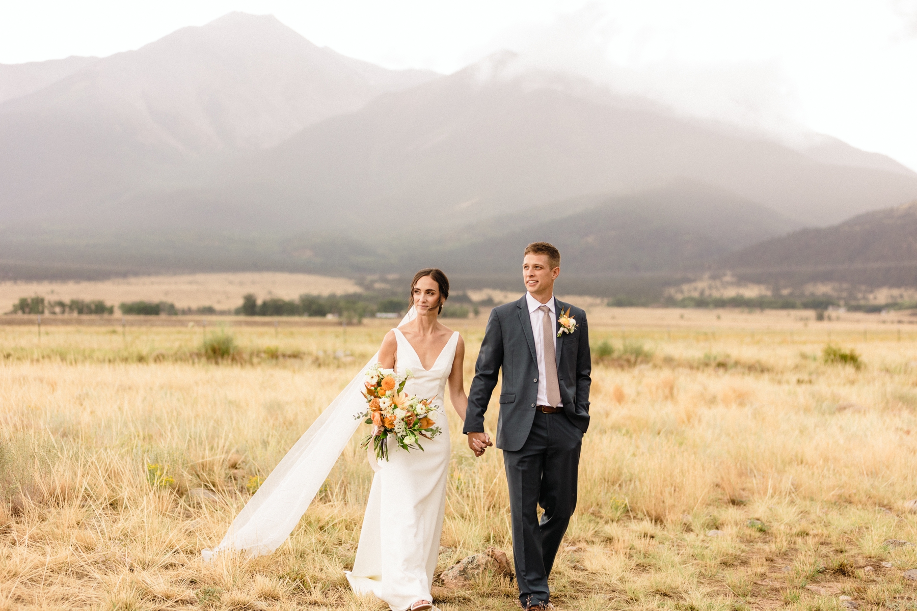 Bride and groom holding hands and walking in field in Colorado 