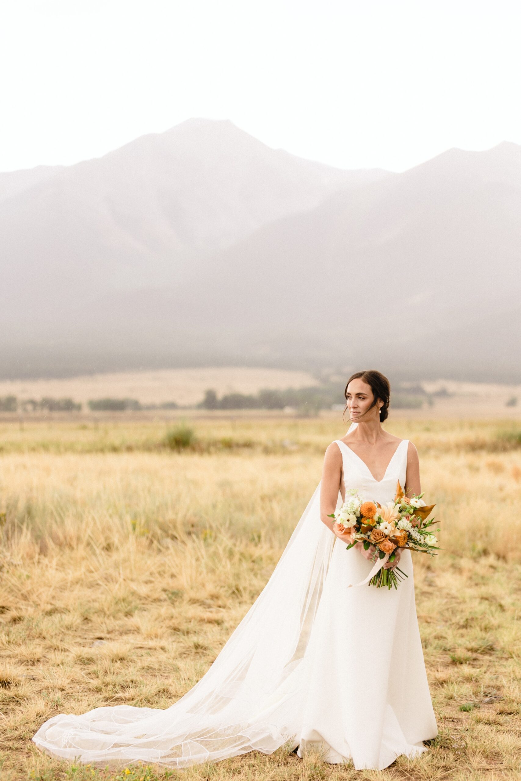 Bride holding bouquet and looking off into the distance in field in Colorado 