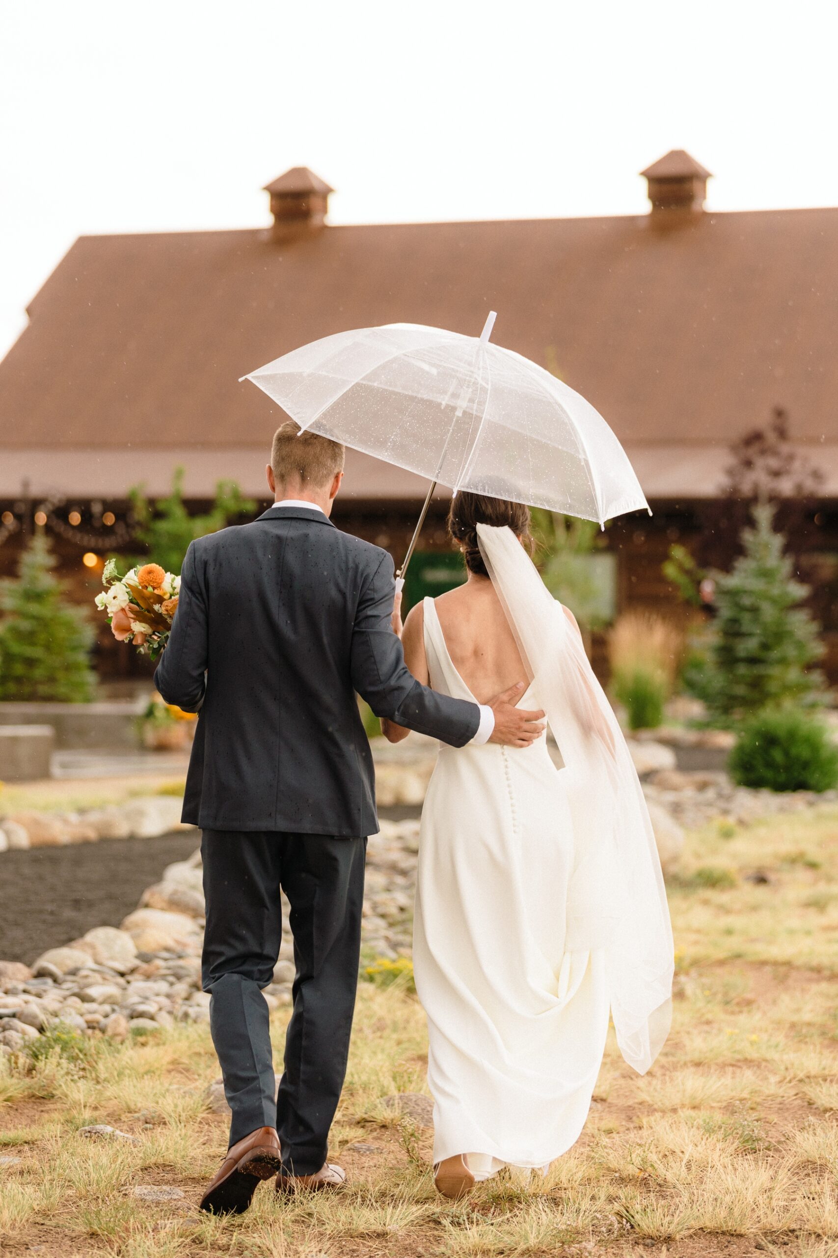 Bride and groom walking under umbrella back