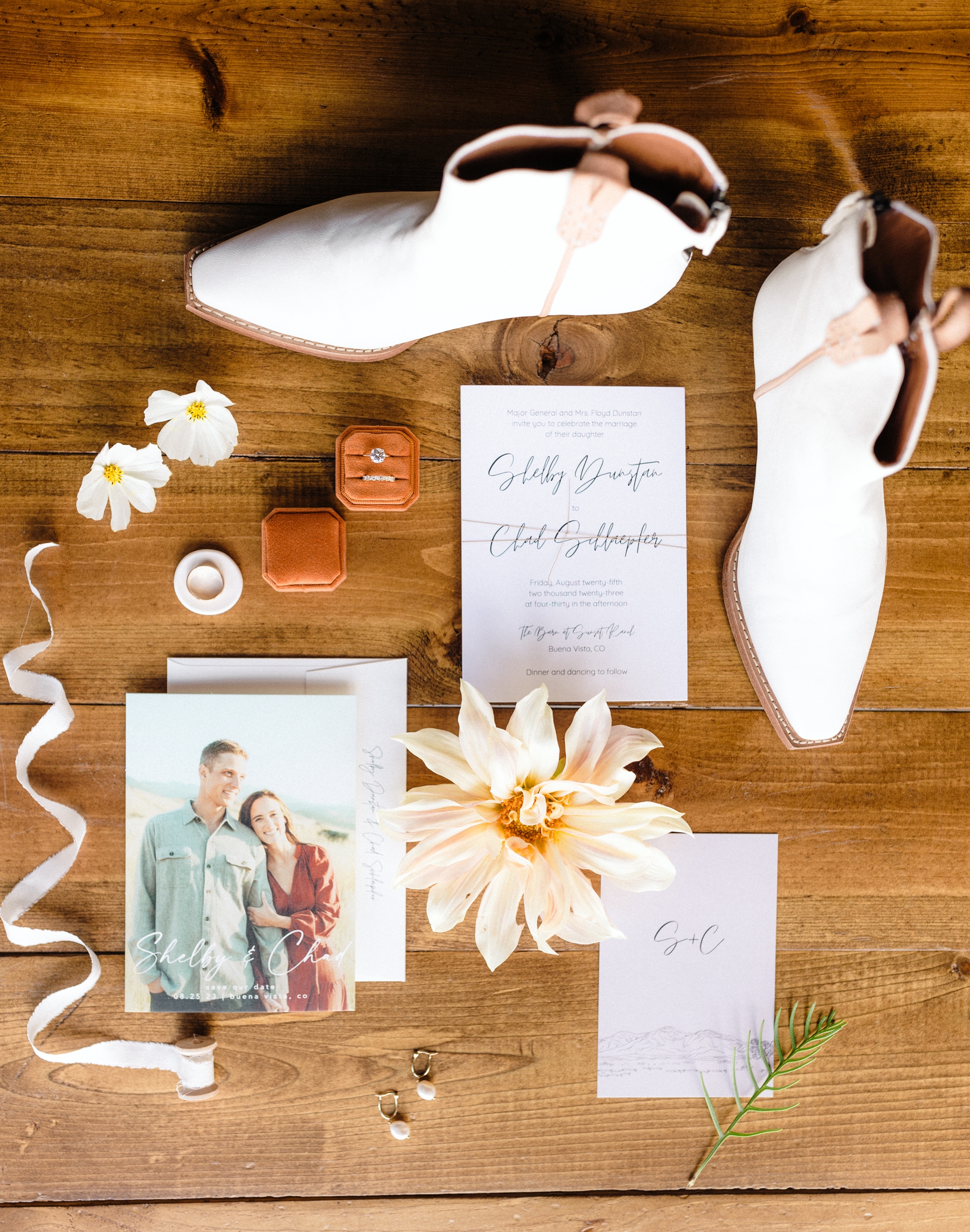 White ankle cowboy boots with white wedding invitation, burnt orange ring box, and flower details 