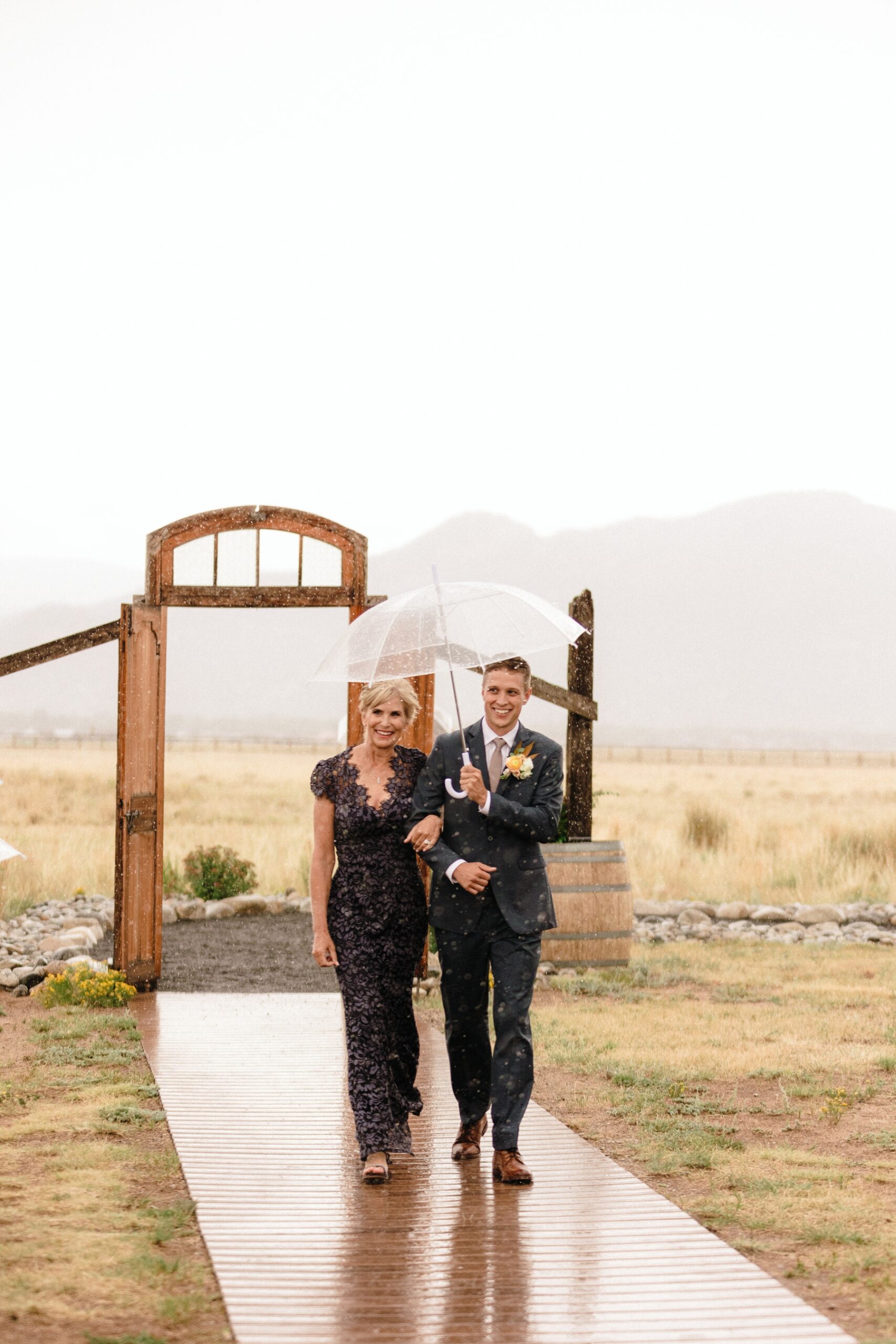 Groom walking down the aisle with mom while it's raining 