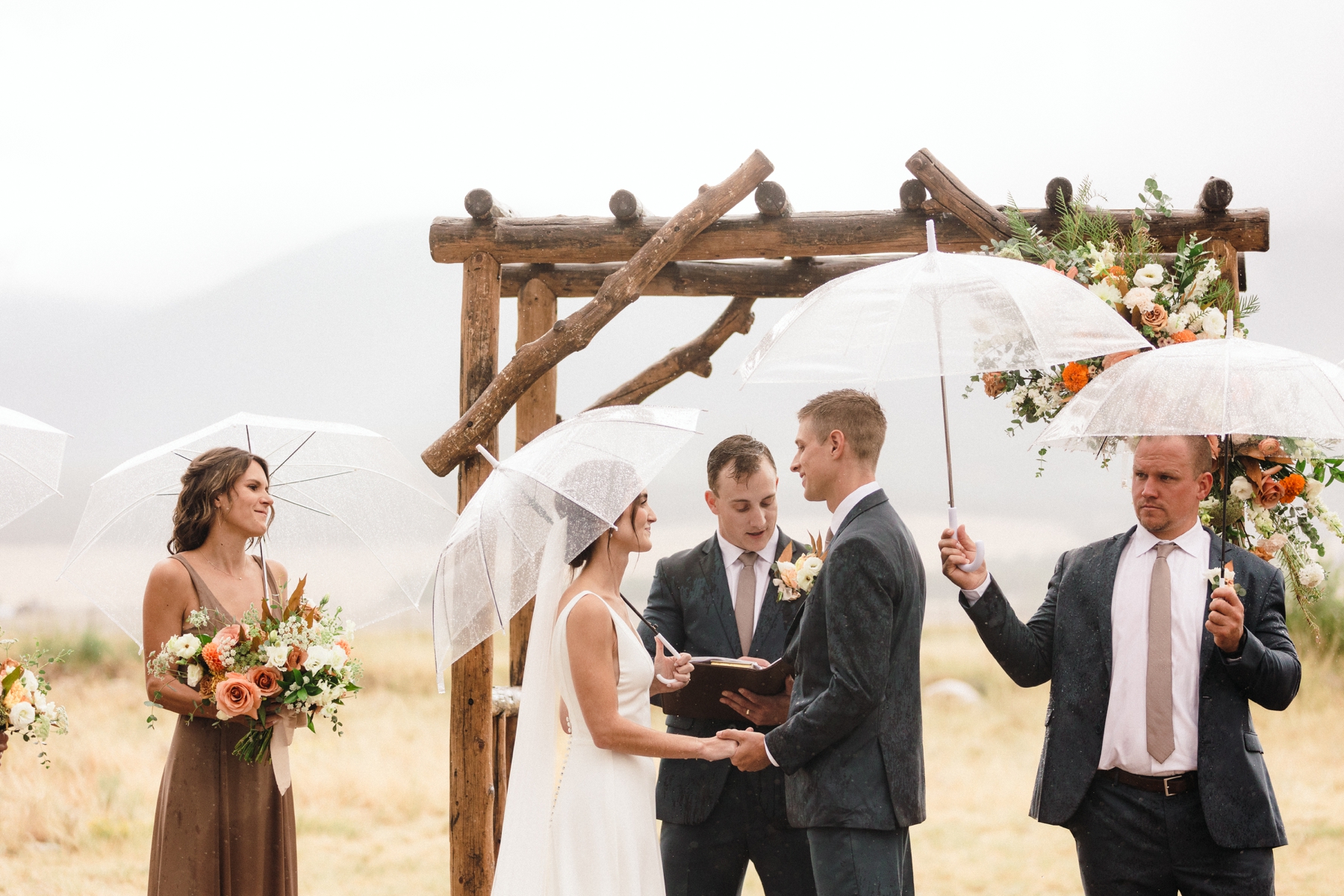 Bride and groom holding hands during ceremony at The Barn at Sunset Ranch while it rains 