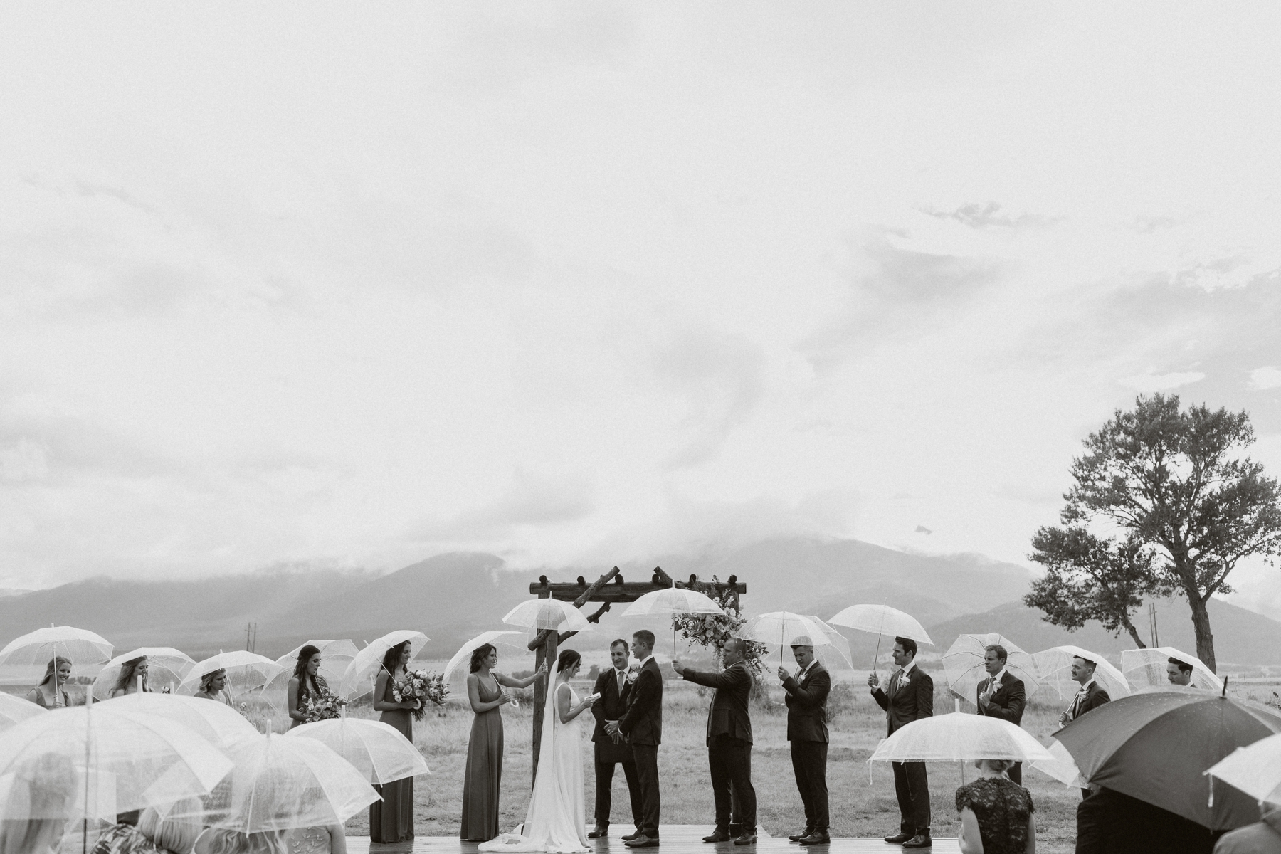 Bride and groom standing at altar with wedding party under umbrellas at The Barn at Sunset Ranch