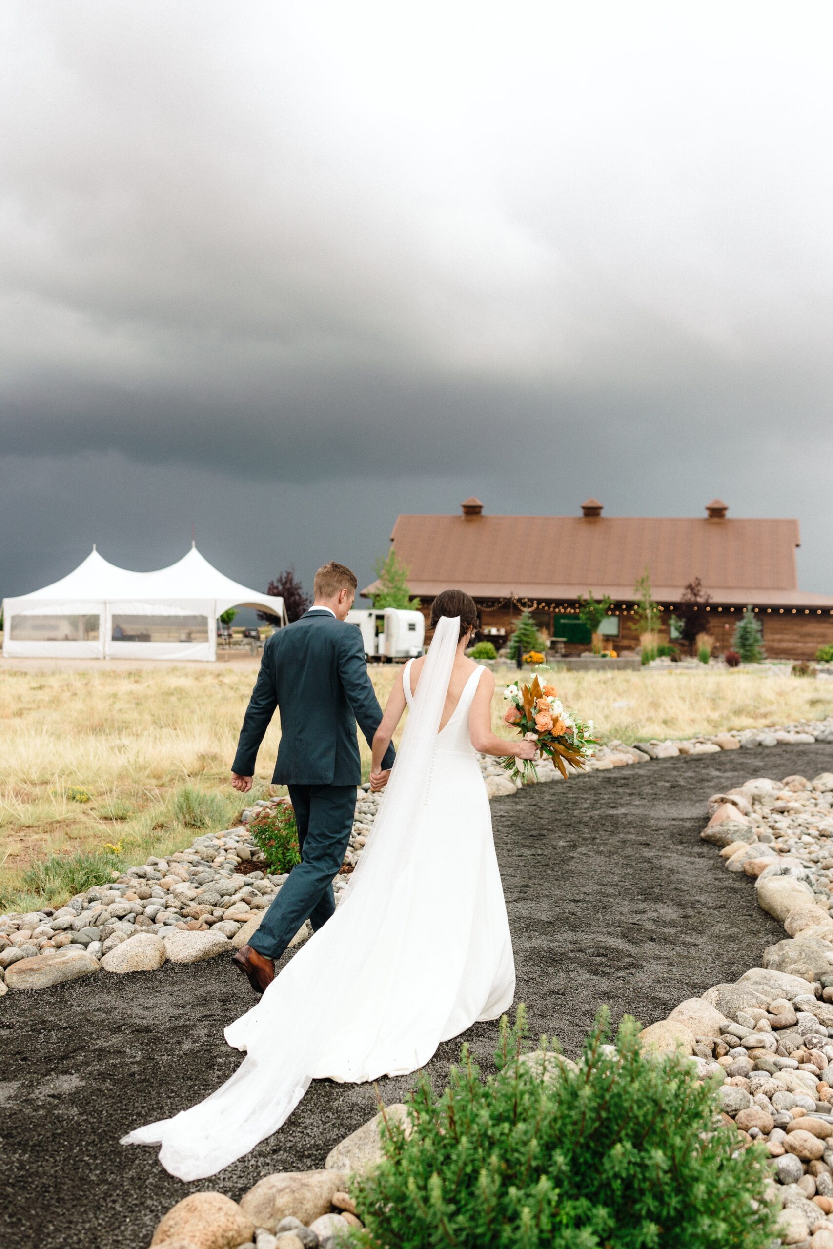 Bride and groom holding hands and walking down path with rain clouds in the background 