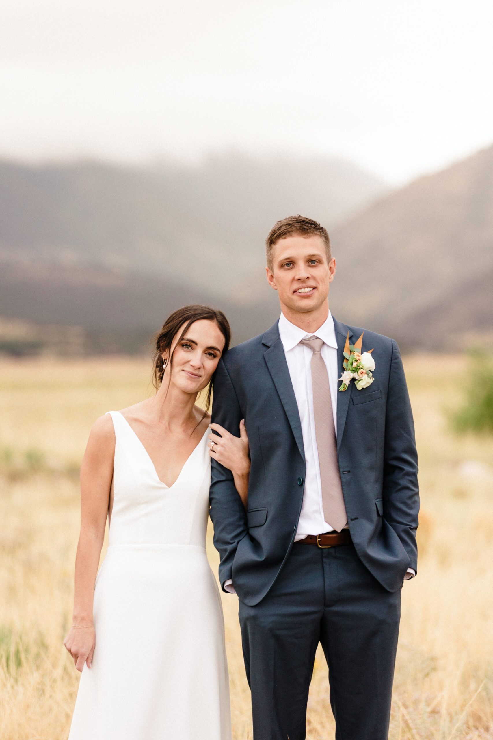 Bride leaning her head against groom's shoulder while standing in a field